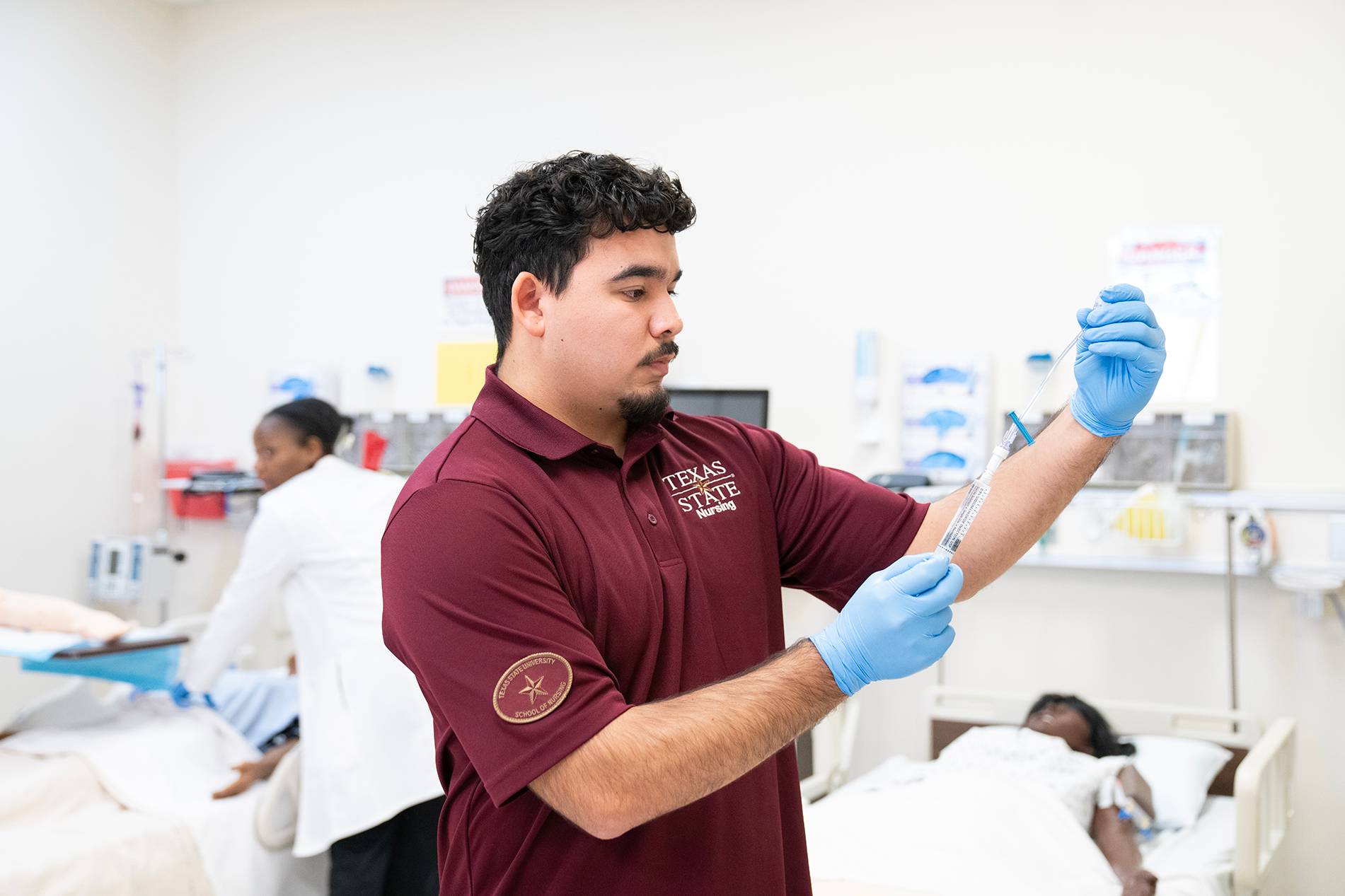 hispanic male looks at medical device while wearing blue latex gloves in hospital room setting
