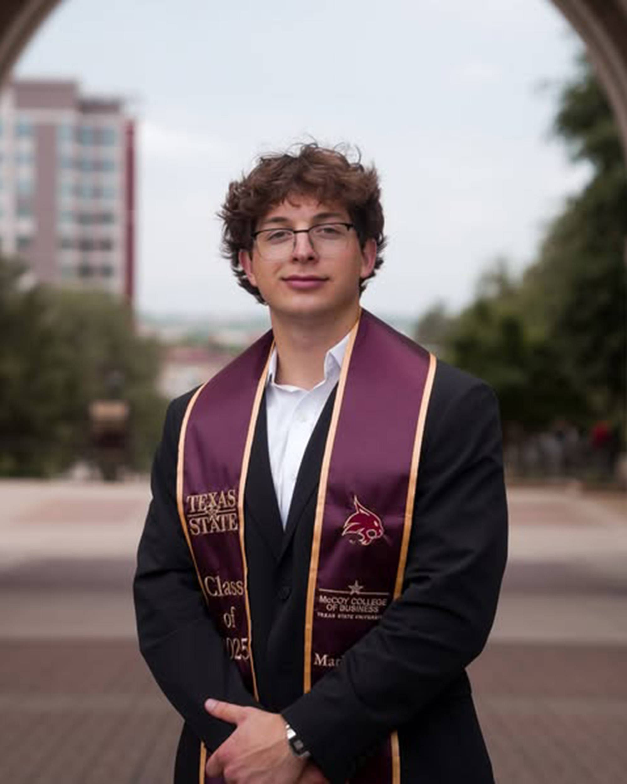 Young man posing outdoors wearing graduation stole