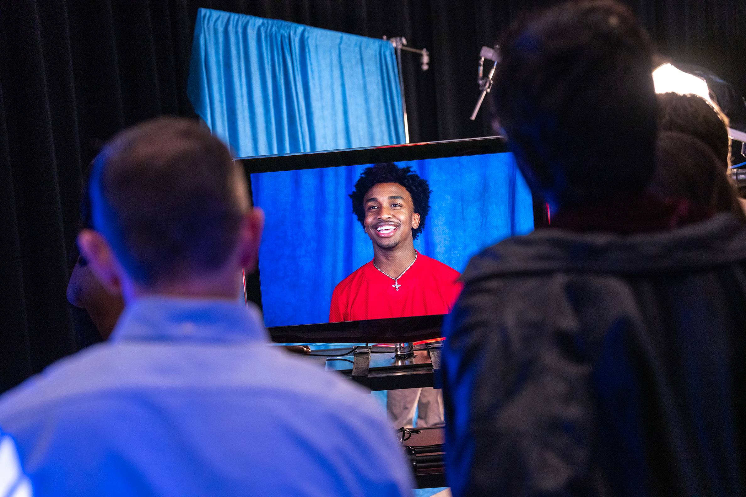 two men watch a large monitor showing an actor