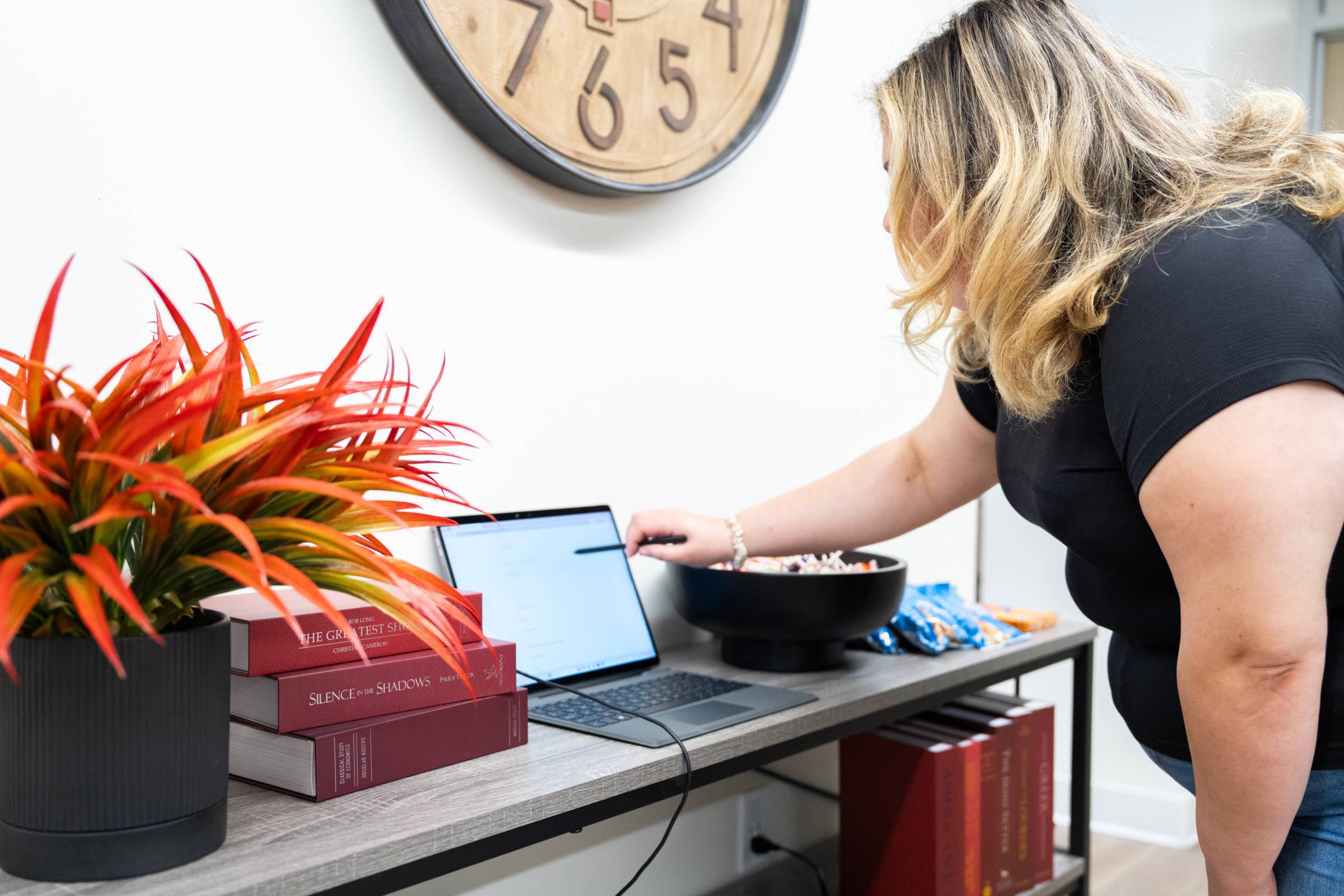 A woman leans forward with a stylus in her hand which is touching the screen of a propped-up tablet.
