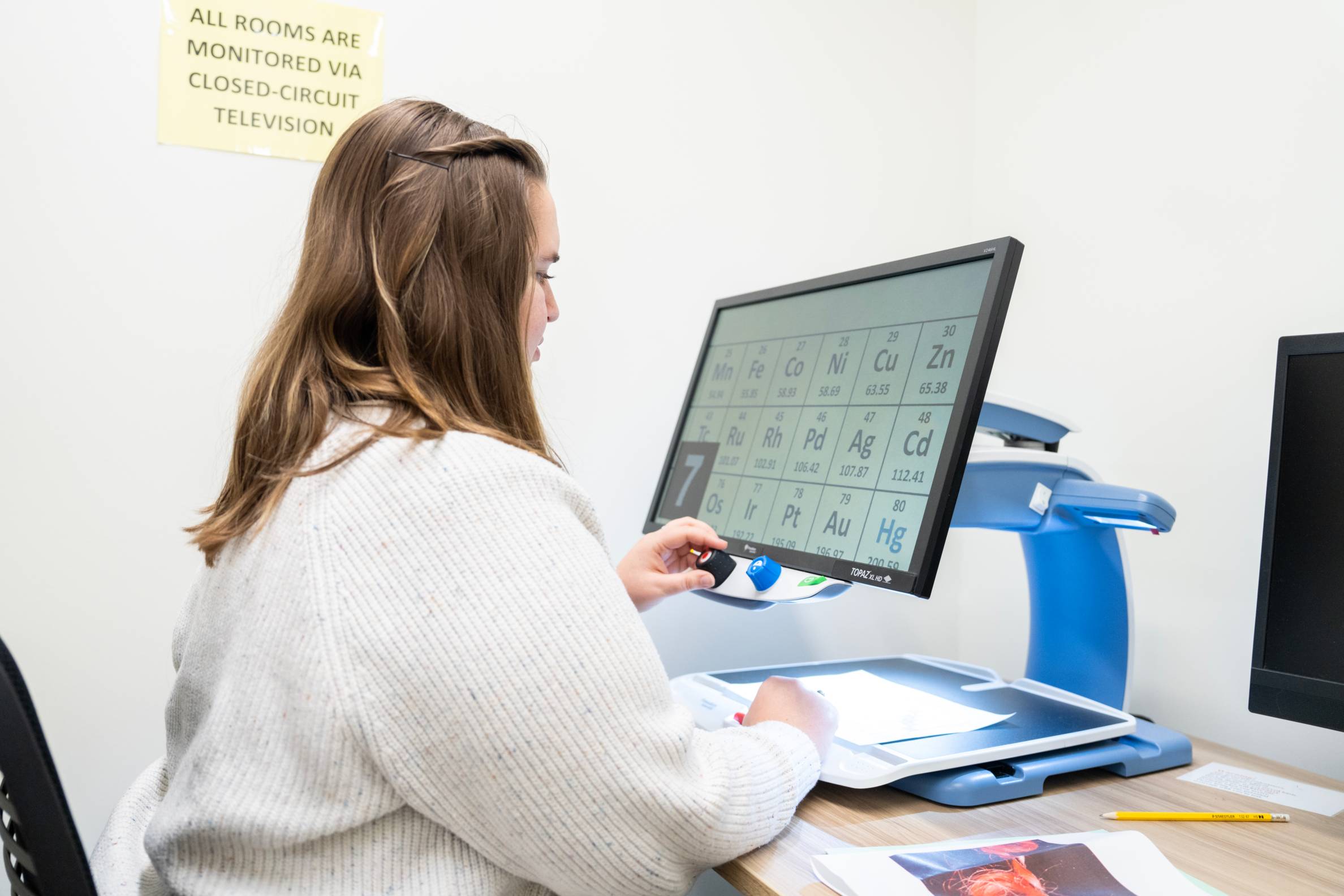 A student is sitting down, utilizing a CC TV screen magnification device.