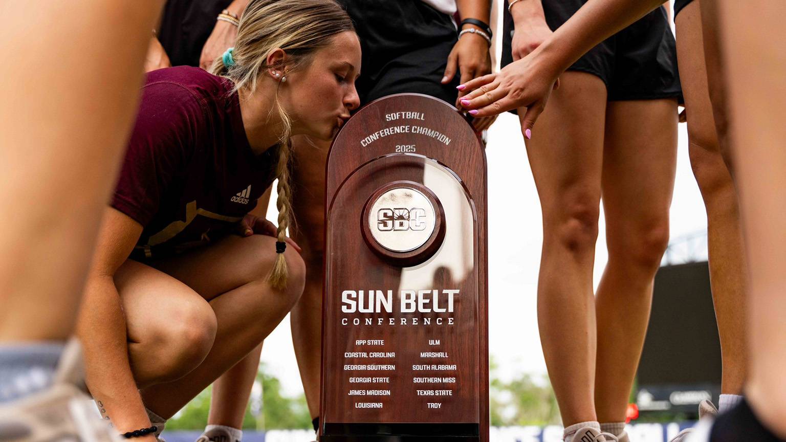 A Bobcat softball player kisses the Sun Belt trophy.