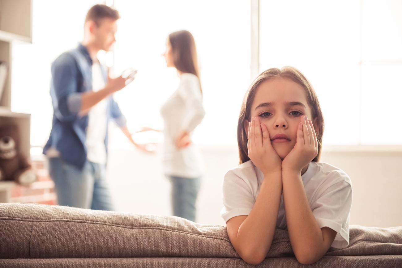A child sits with her head in her hands while her parents argue in the background