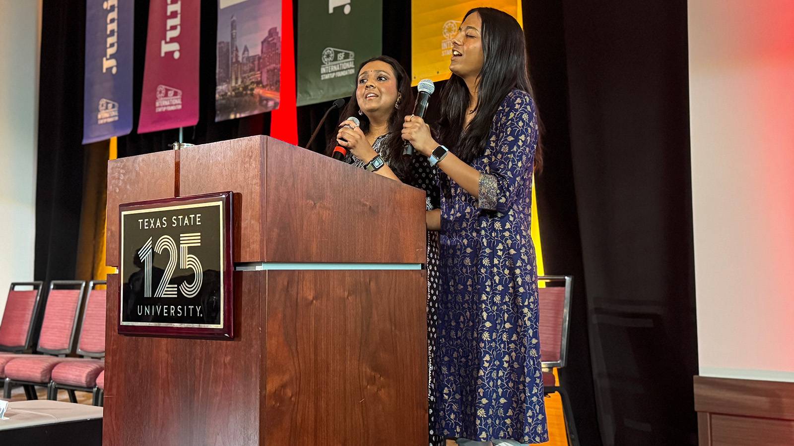 two women singing at a podium on stage