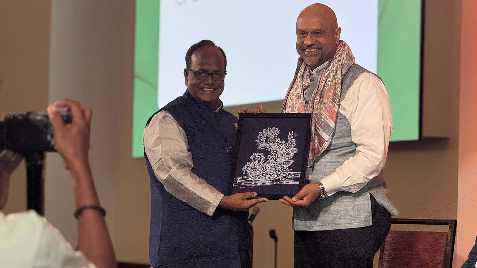 two men posing for a photo as one gifts the other framed art