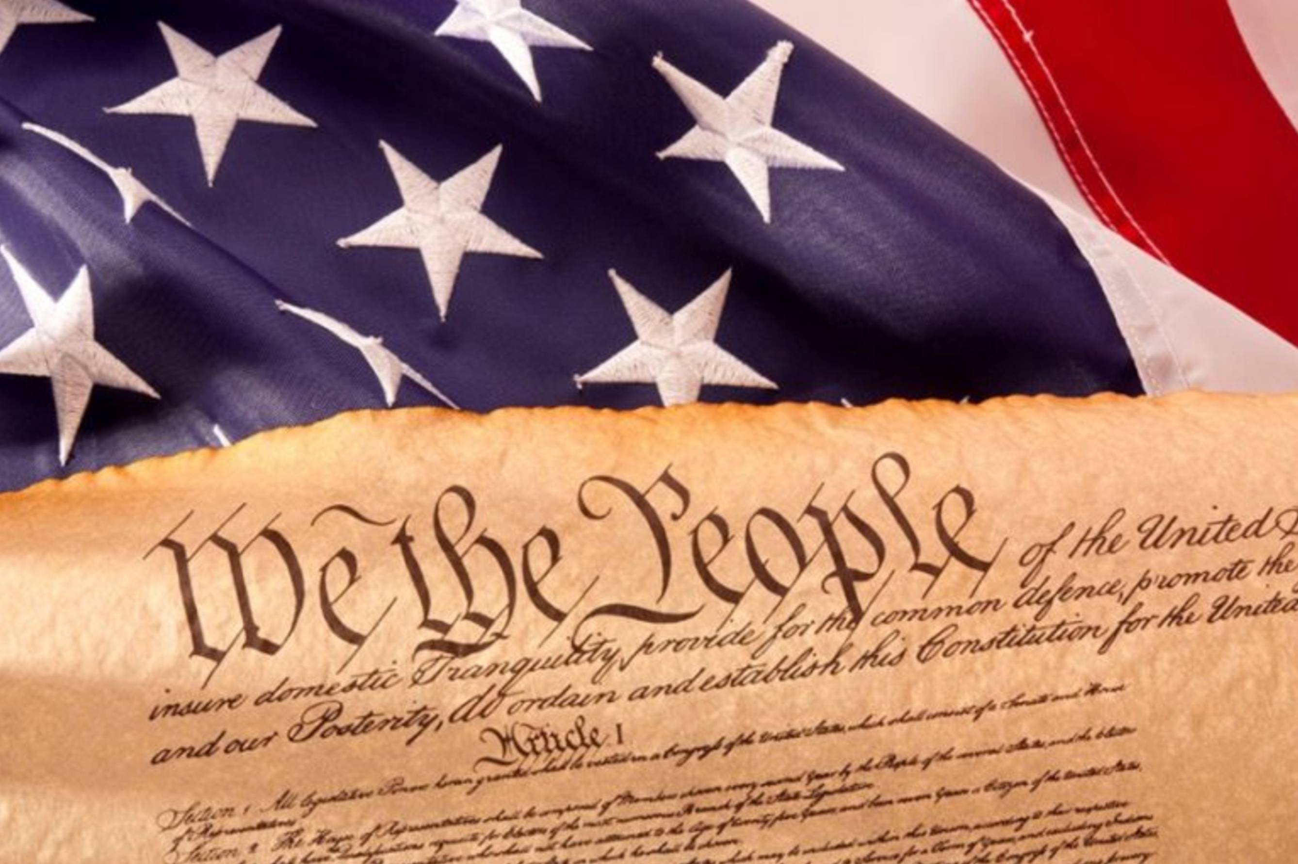 image of the top portion of the US Constitution with a flag behind it