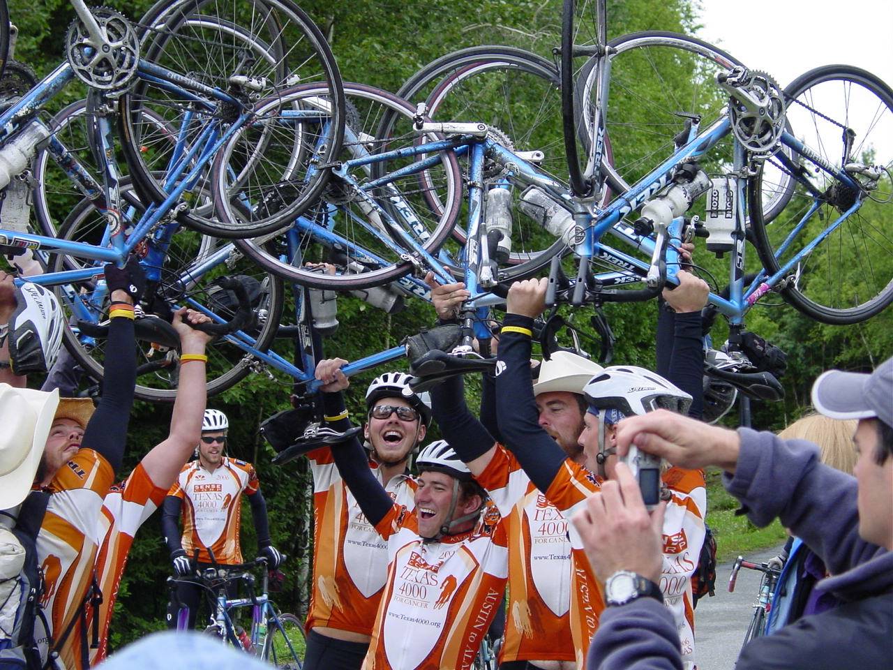 Rob Landauer celebrates finishing the Texas 4,000 with a group of cyclists, lifting their bikes over their heads in victory as they cheer.