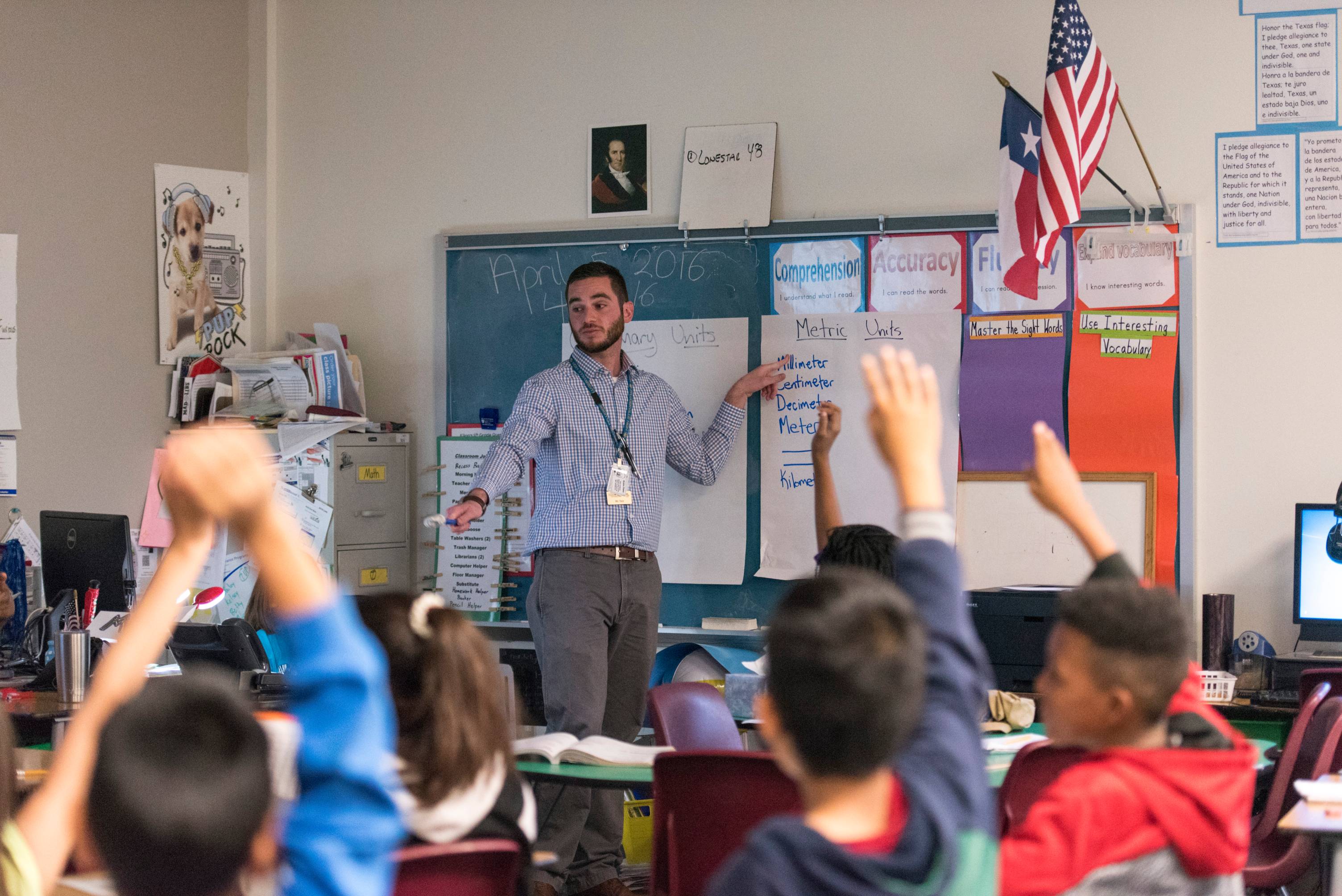 Students raising their hands to be called on by teacher. 
