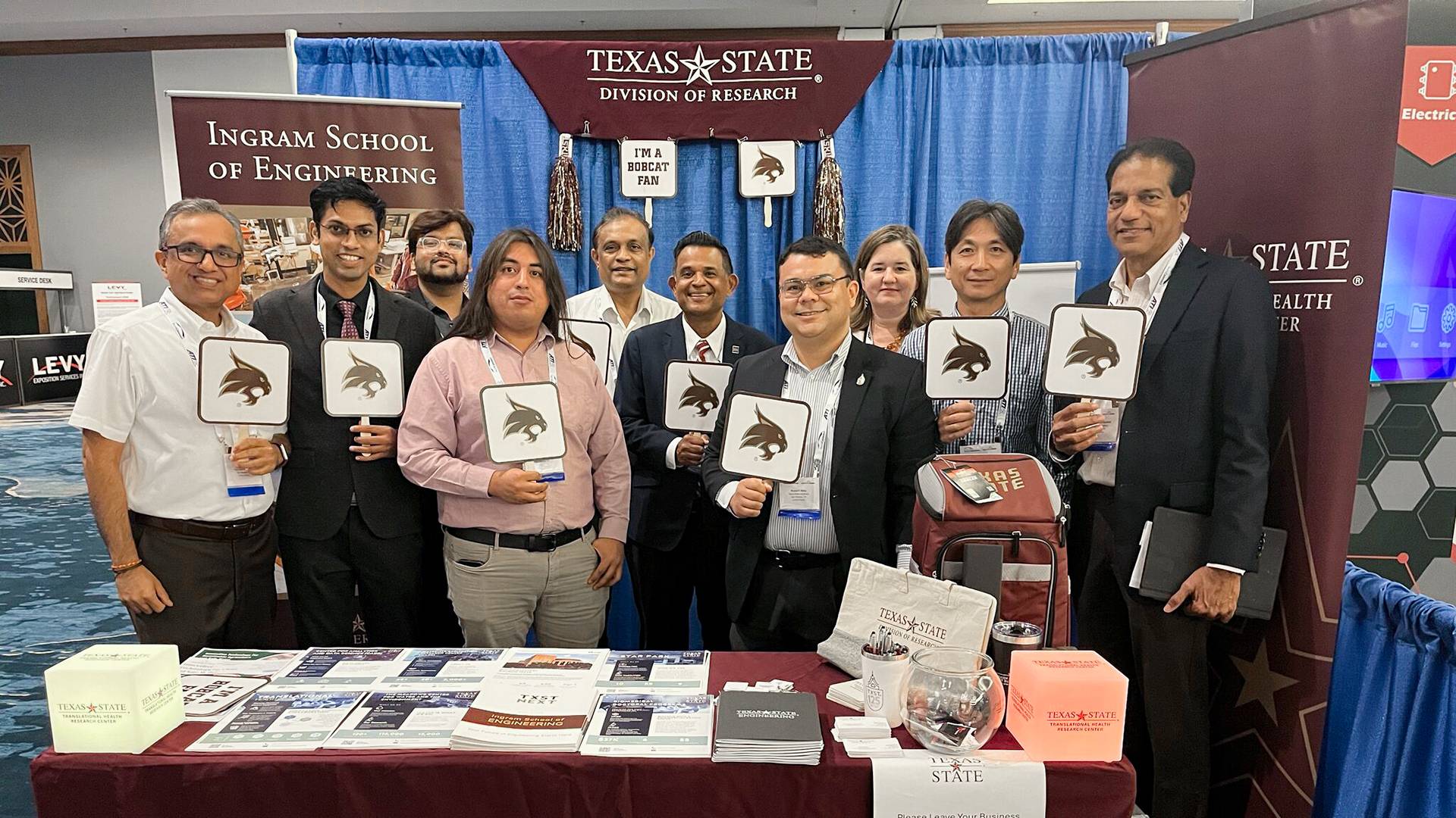conference attendees taking a group photo next to an information booth