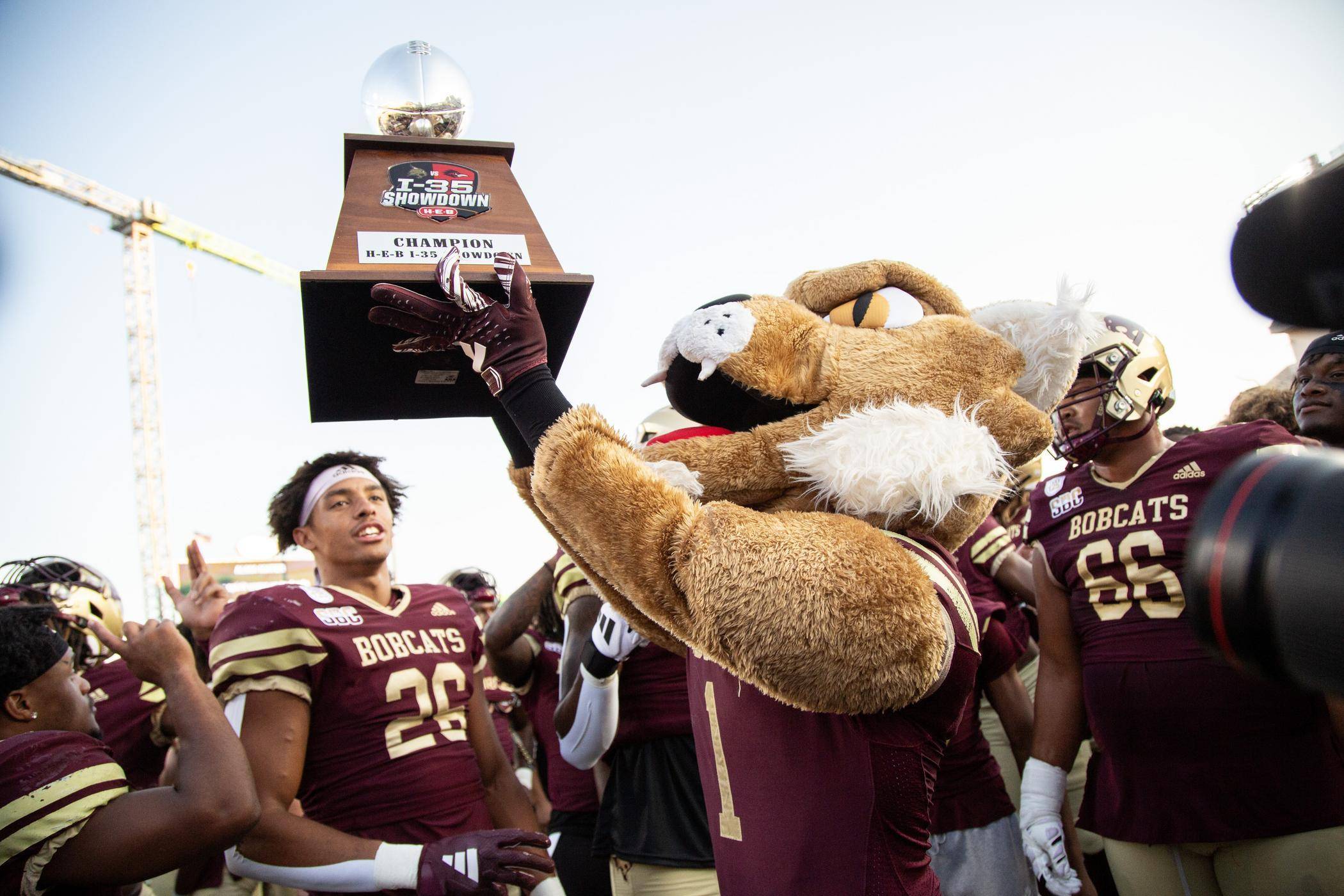 boko the bobcat mascot holding up a championship trophy while surrounded by football players