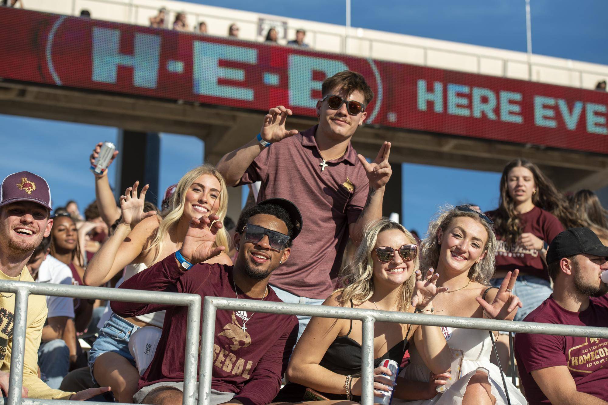 large group of students at football game holding up txst hand signs