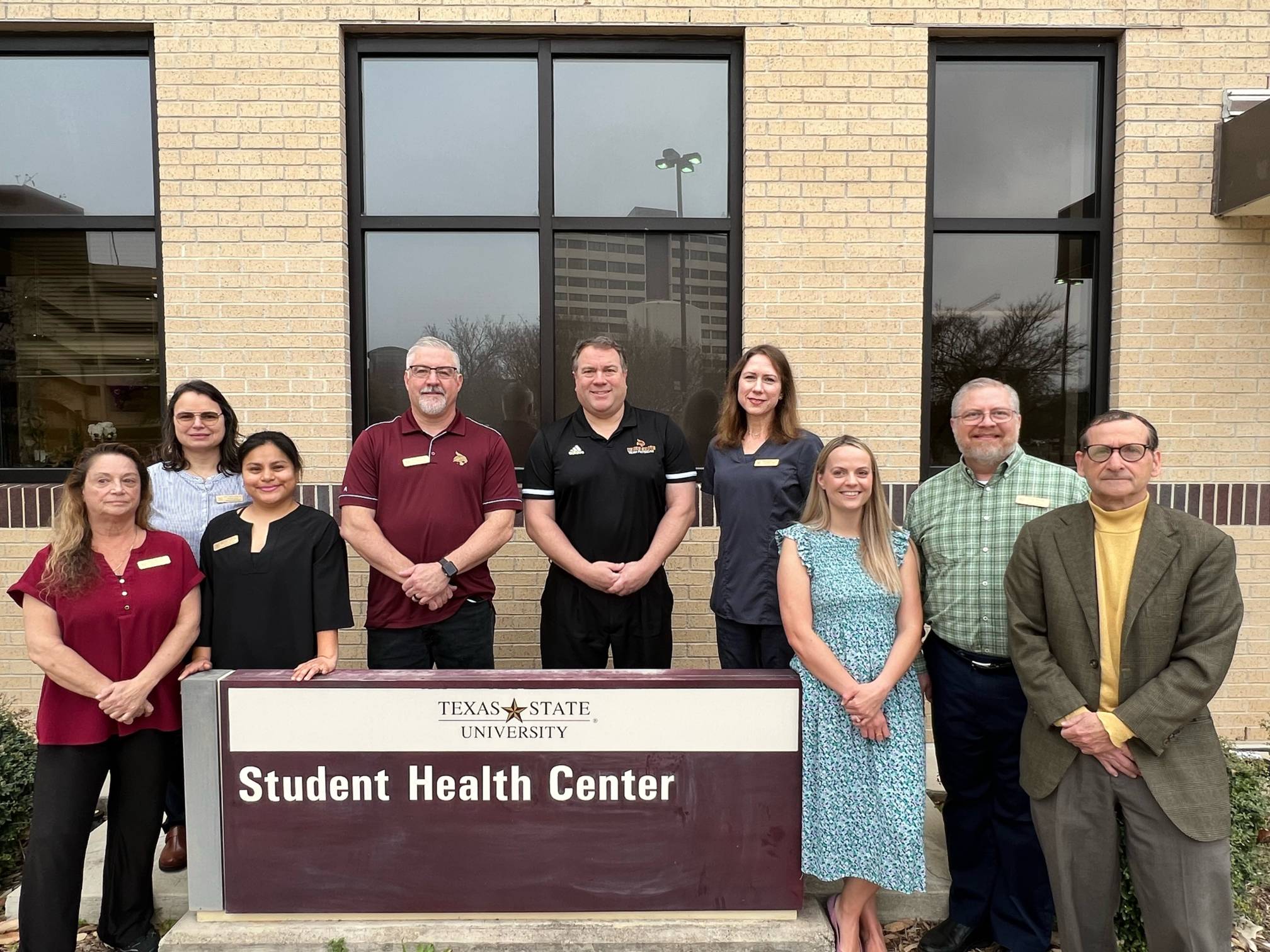 Photo of the Student Health Center close up with providers standing outside, smiling.