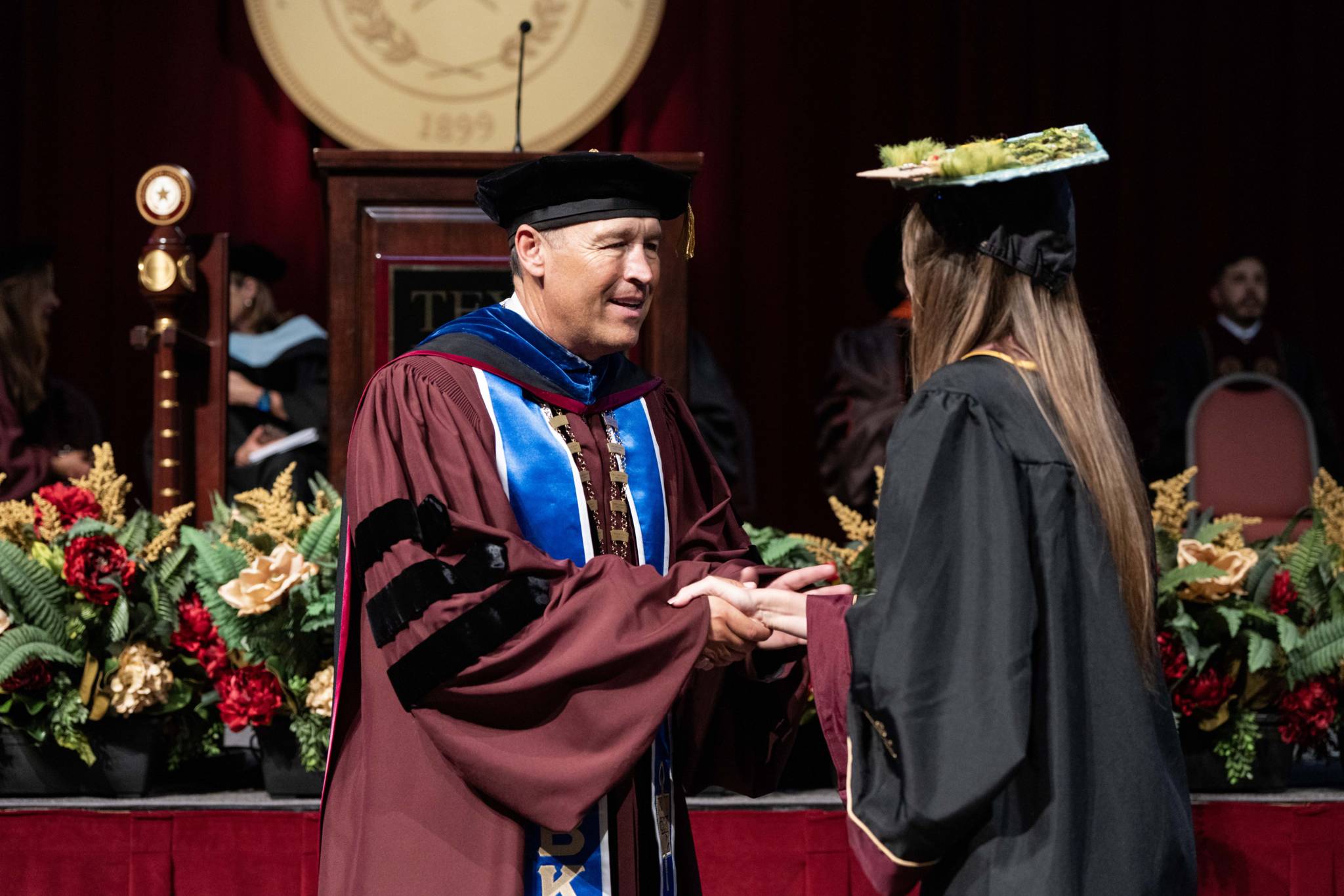 TXST President Damphousse shaking hands with student as they cross the stage for graduation.