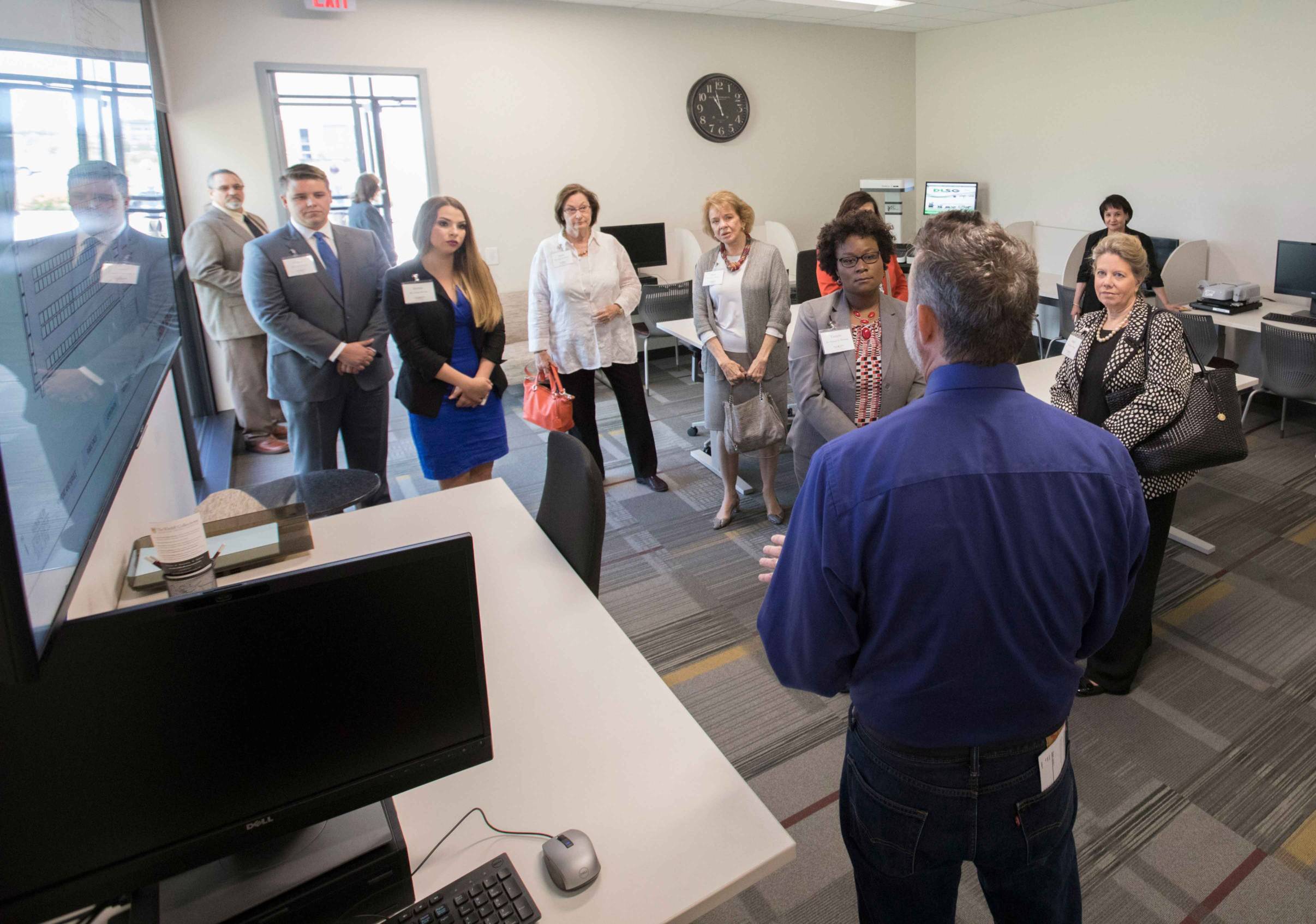 A group of people stands in an office while a man in a blue shirt speaks to them.