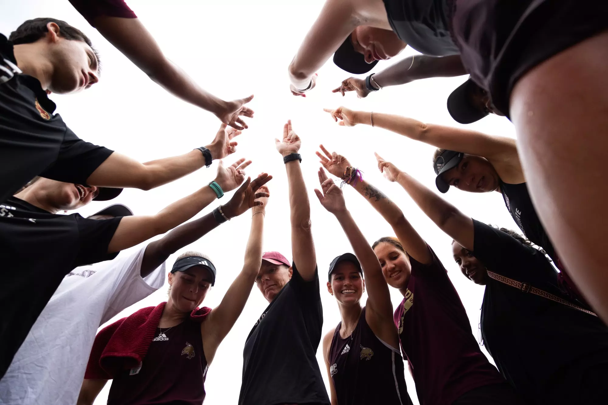 female tennis players gather in circle with txst hand signs in air