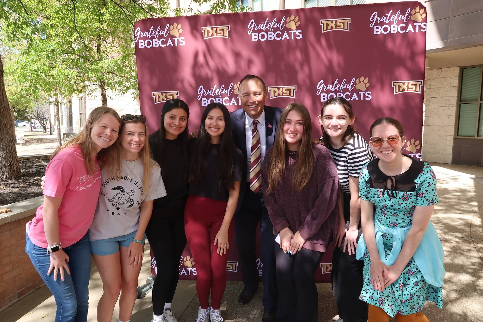 Students with President Damphousse in front of grateful bobcats backdrop