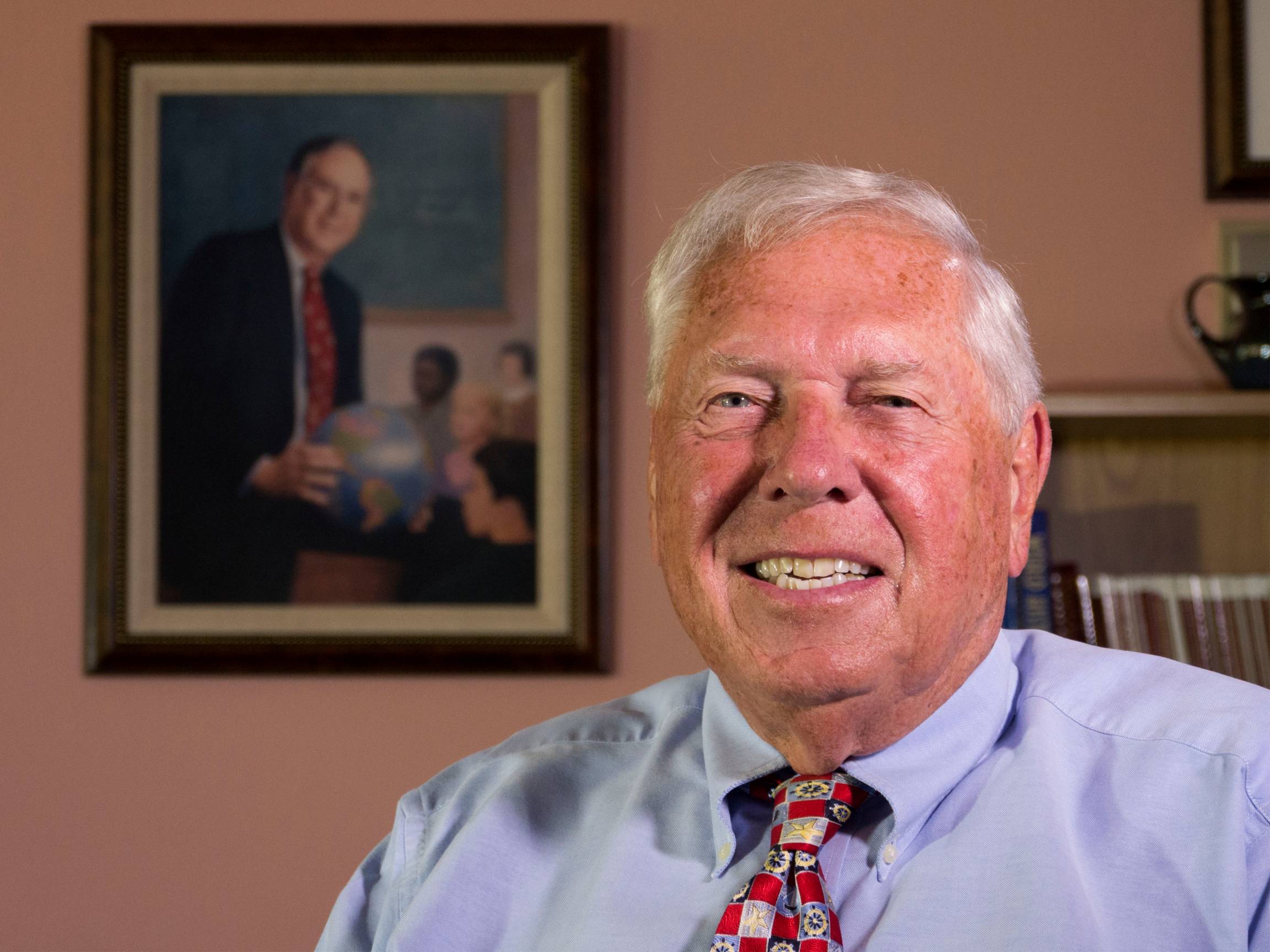 Portrait of Richard Boehm in front of painting of Gil Grosvenor