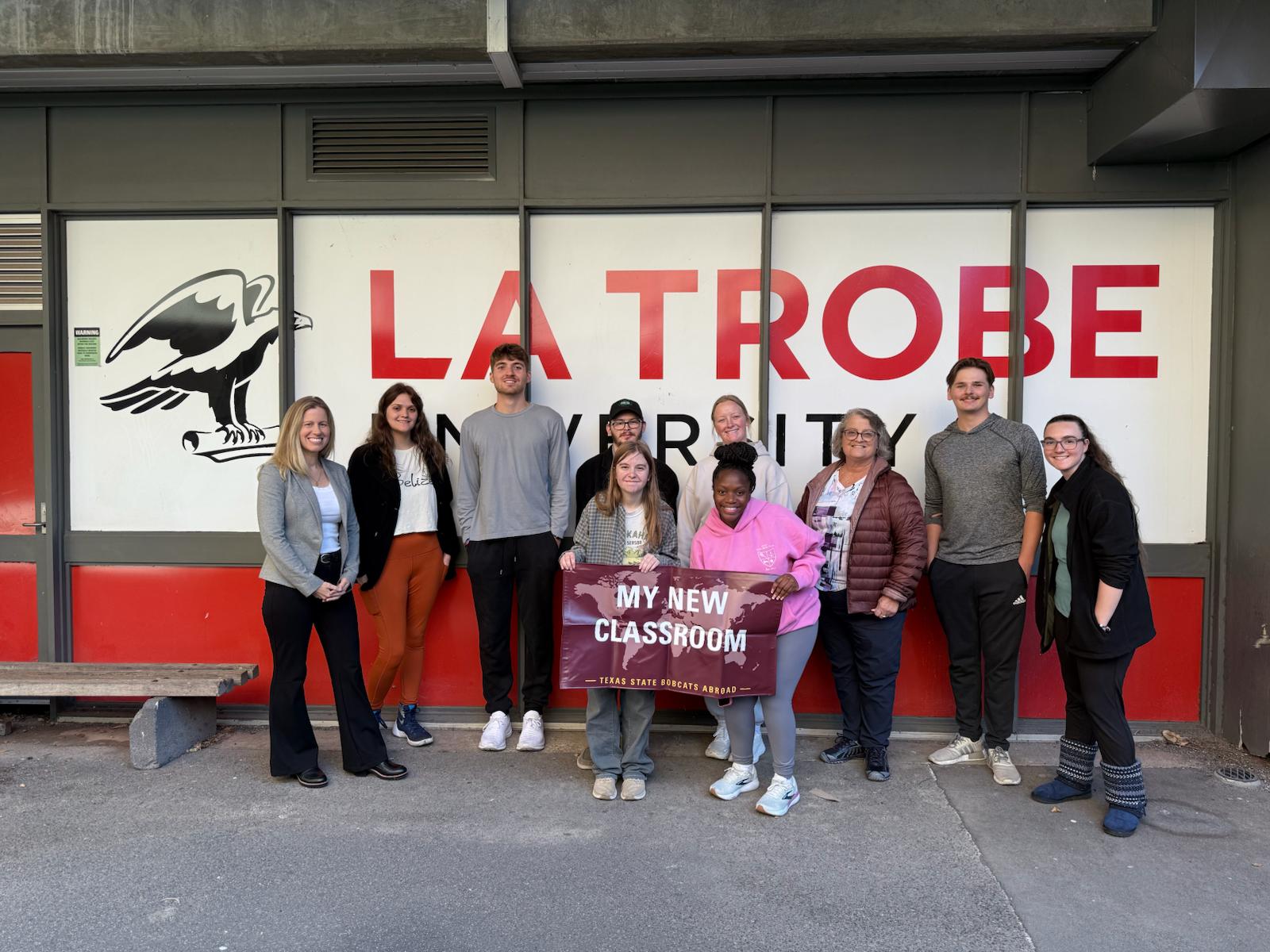 Group of students standing in front of La Trobe banner on campus.