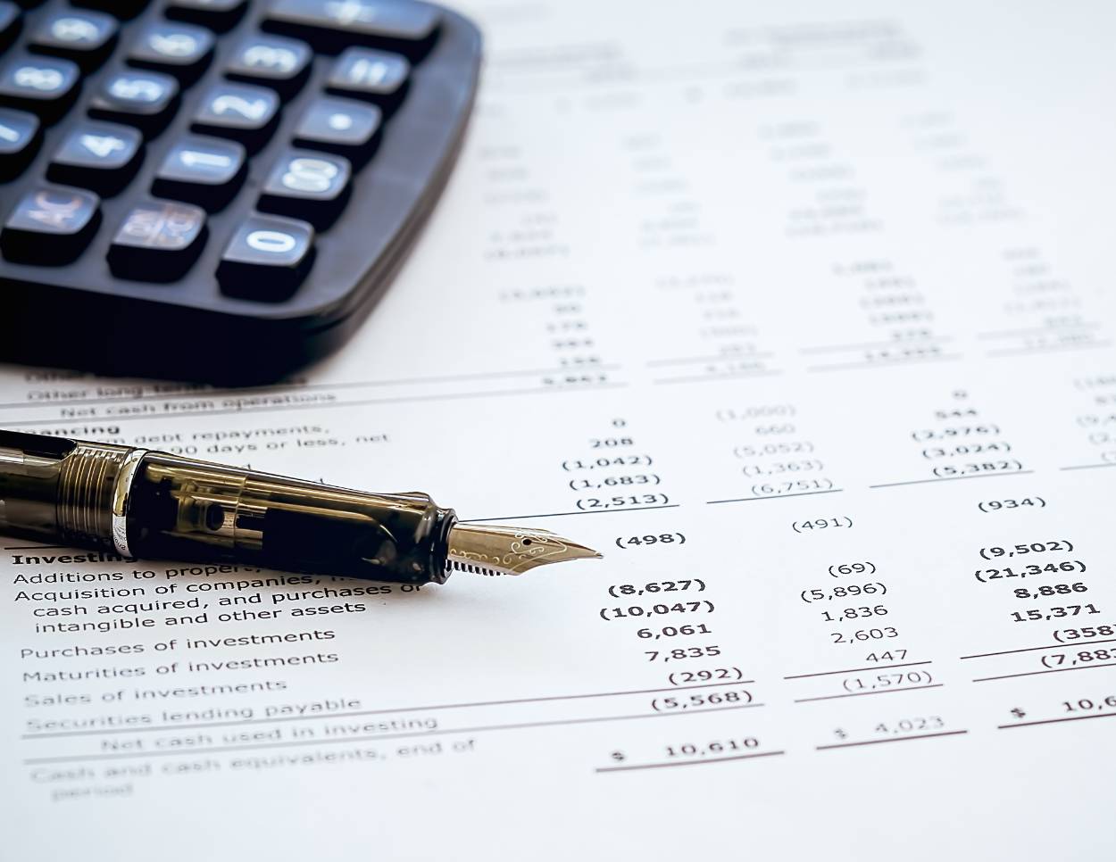 Calculator and fountain pen laying on a white paper balance sheet with figures on it