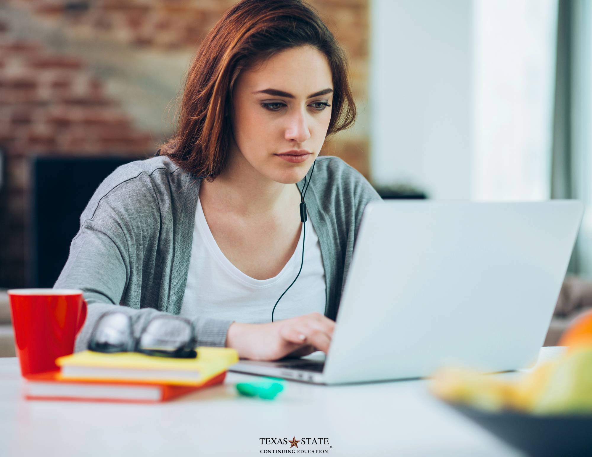 A woman sitting at a table with a red coffee cup engaged in an online course