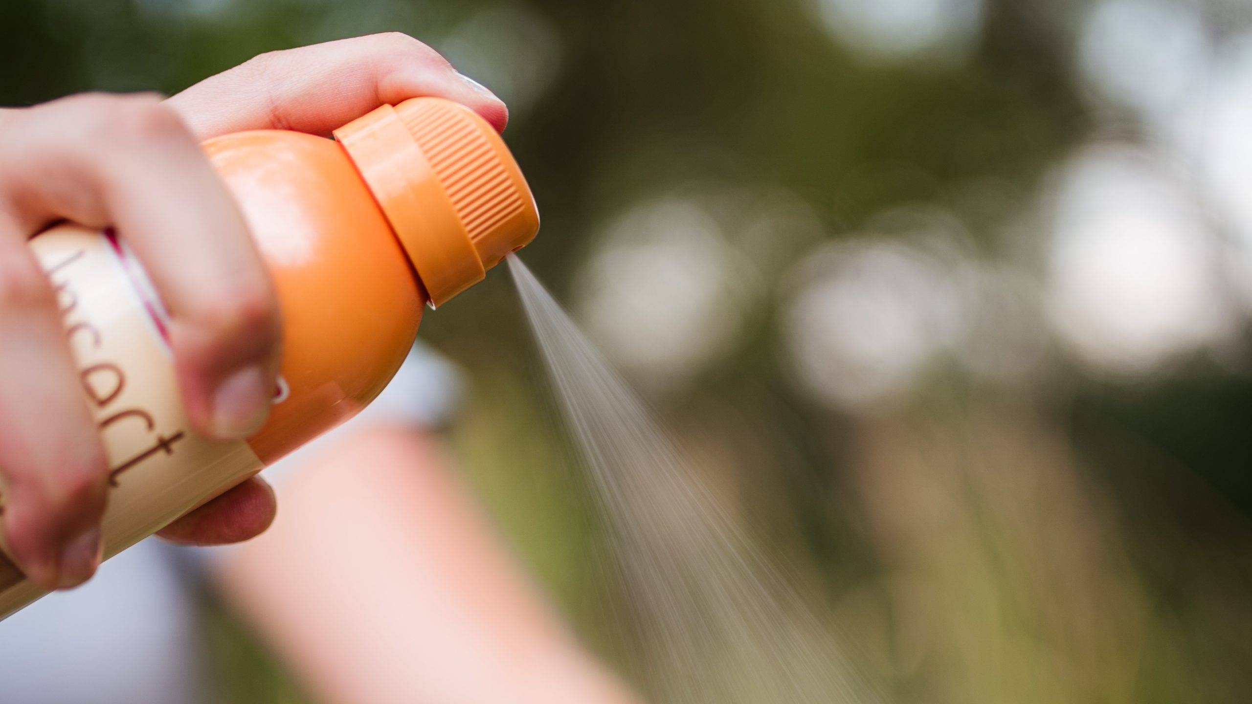 A hand sprays insect repellant spray
