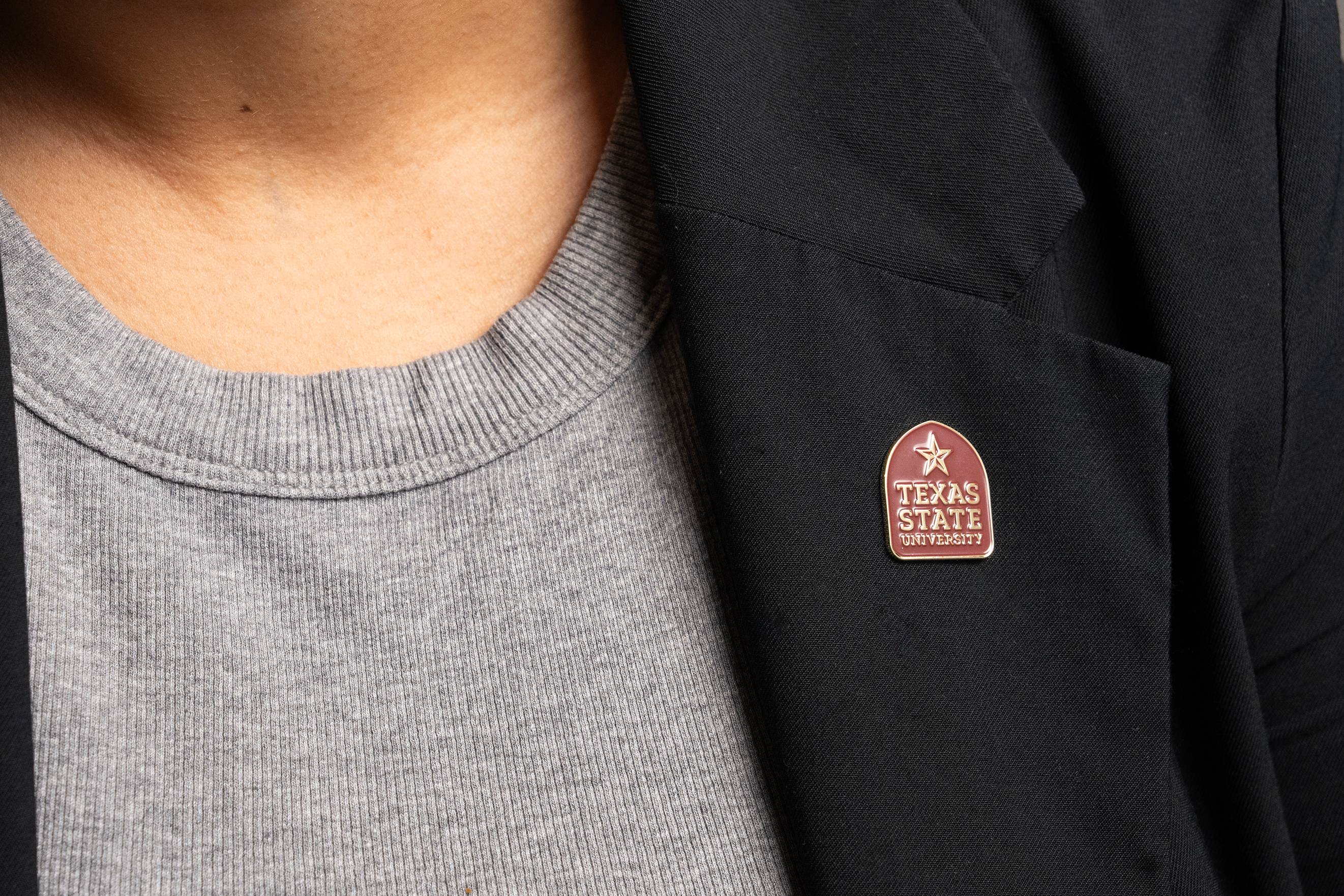 maroon and gold label pin reading "texas state university" on a black blazer