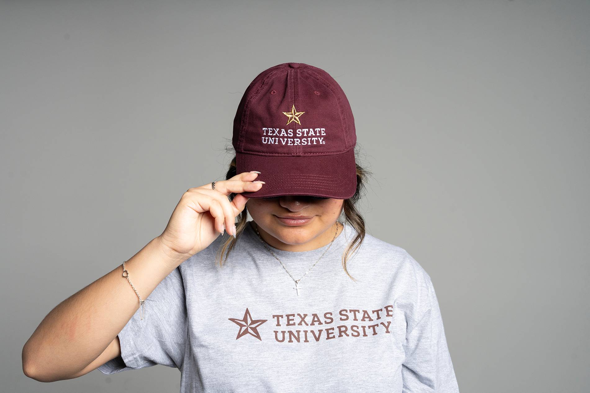woman wearing maroon hat and grey shirt. both read "texas state university"