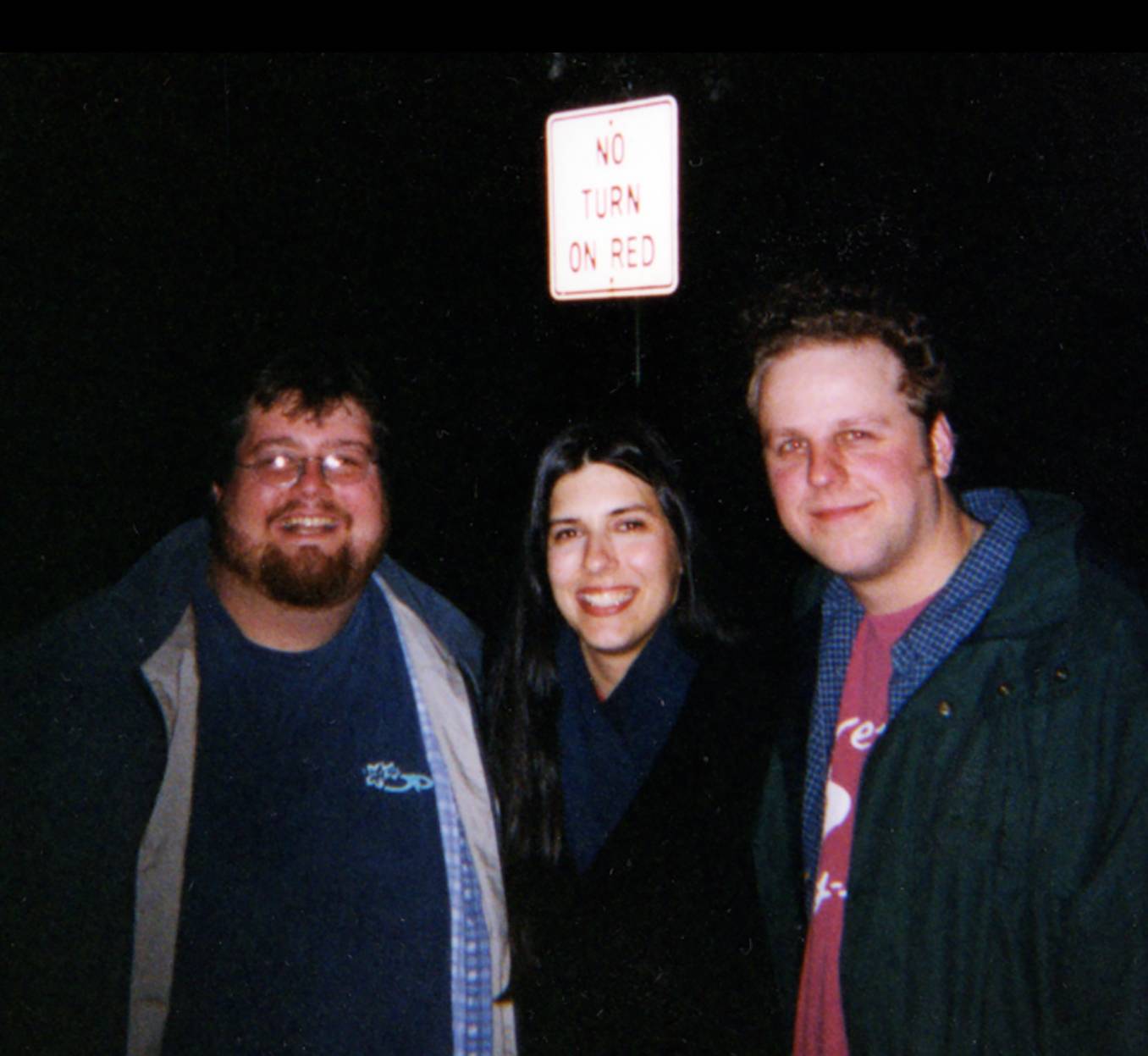 woman and two man posing for photo in front of a sign that reads "no turn on red"