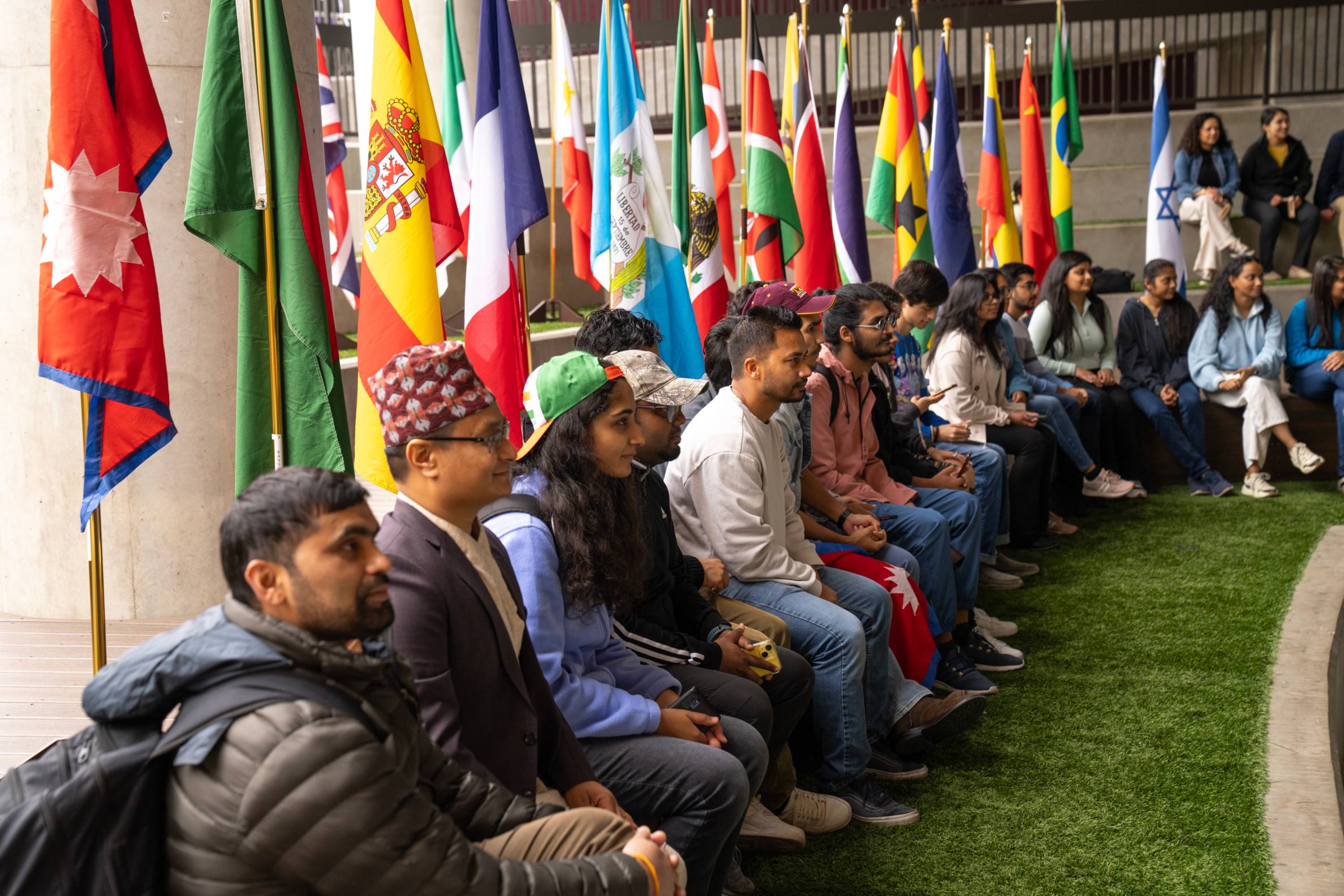 A row of international students seated in front of a row of international flags