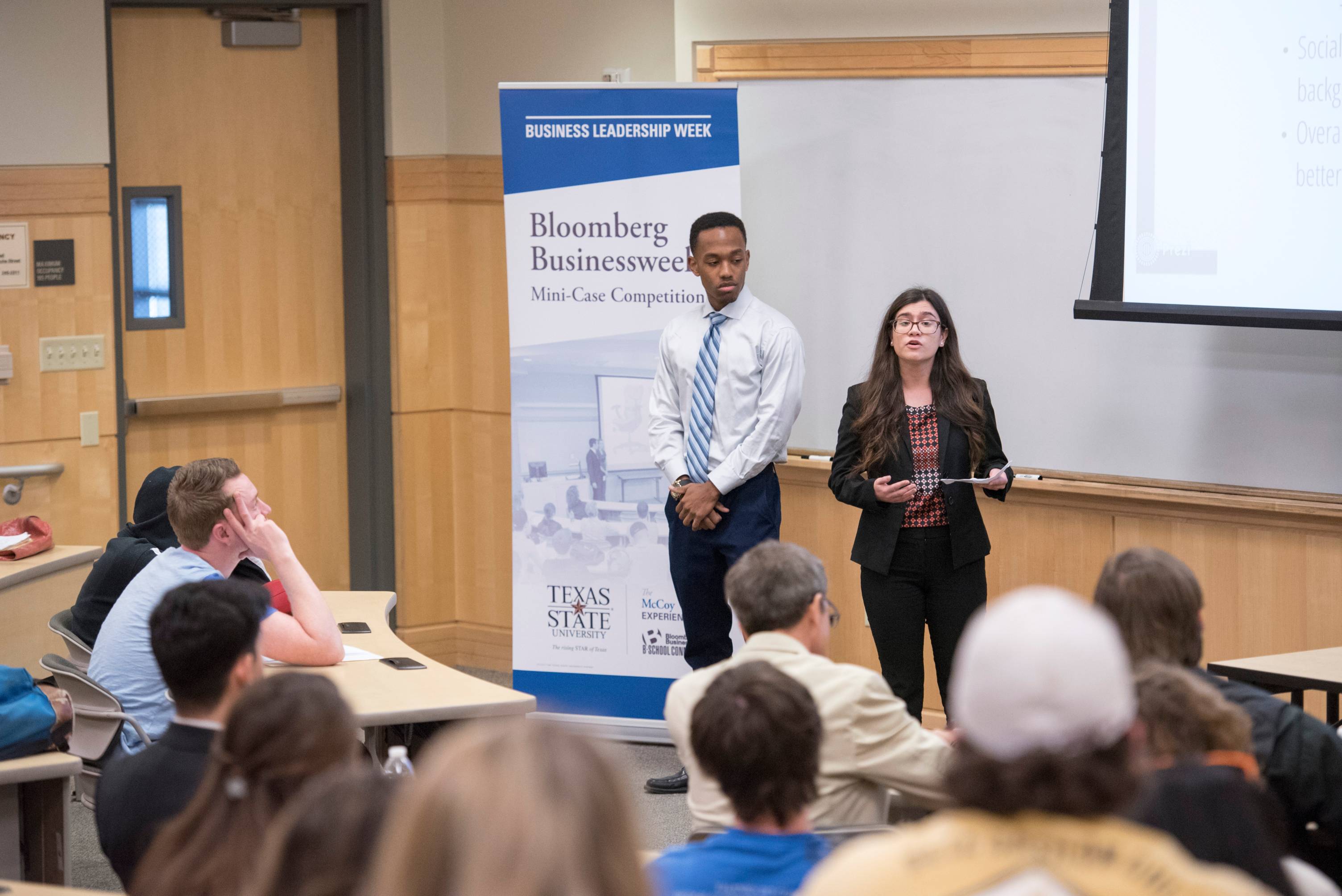 A row of international students seated in front of a row of international flags