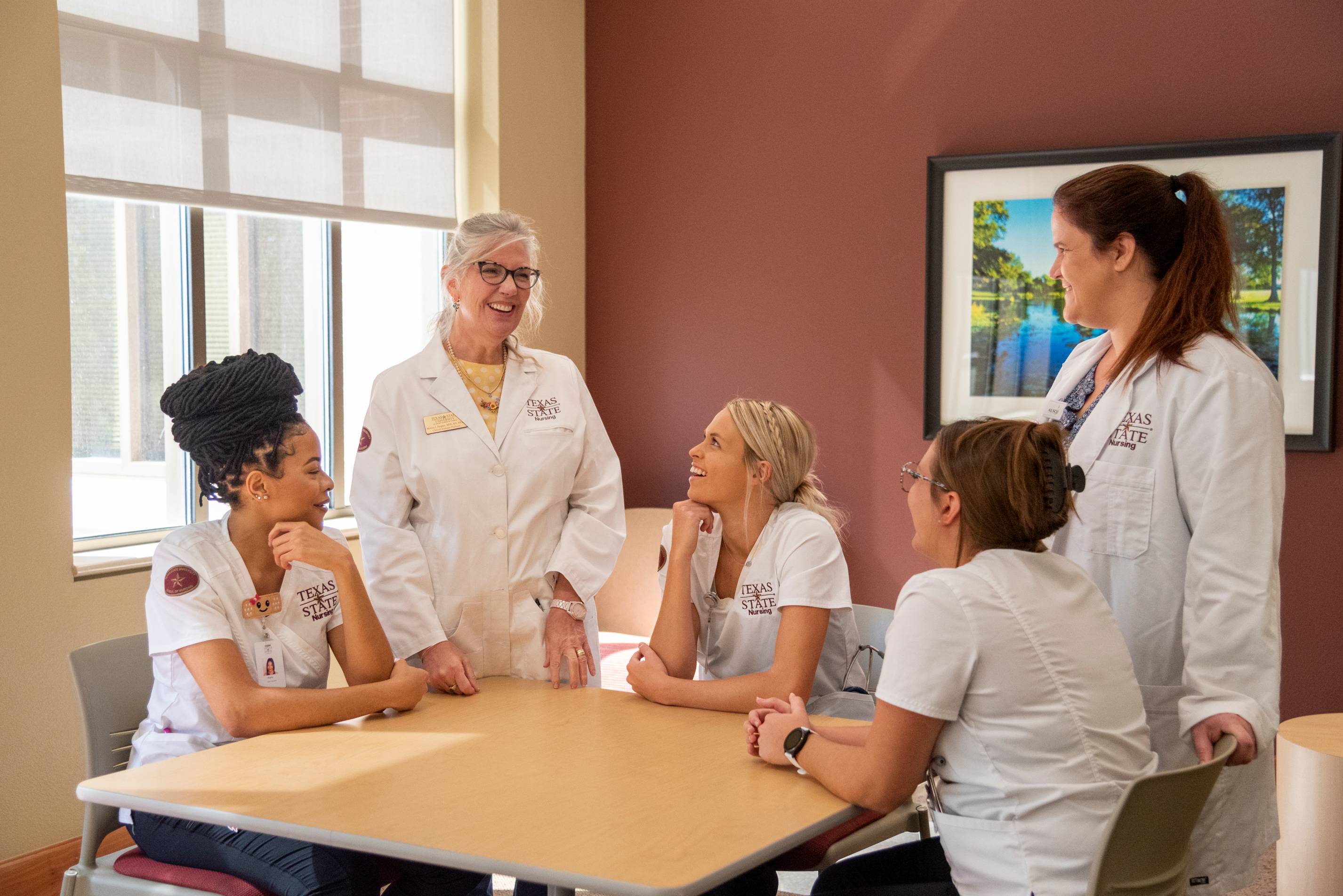 Students gathered around a table listening to teacher talk. 