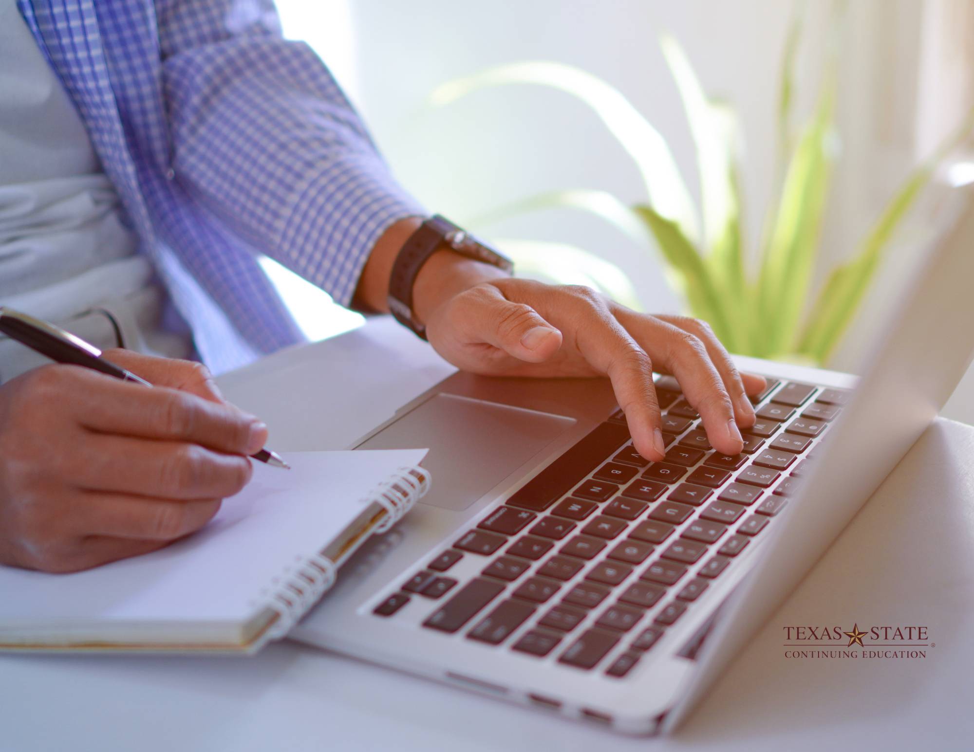 a man types on a laptop while taking notes with a fountain pen