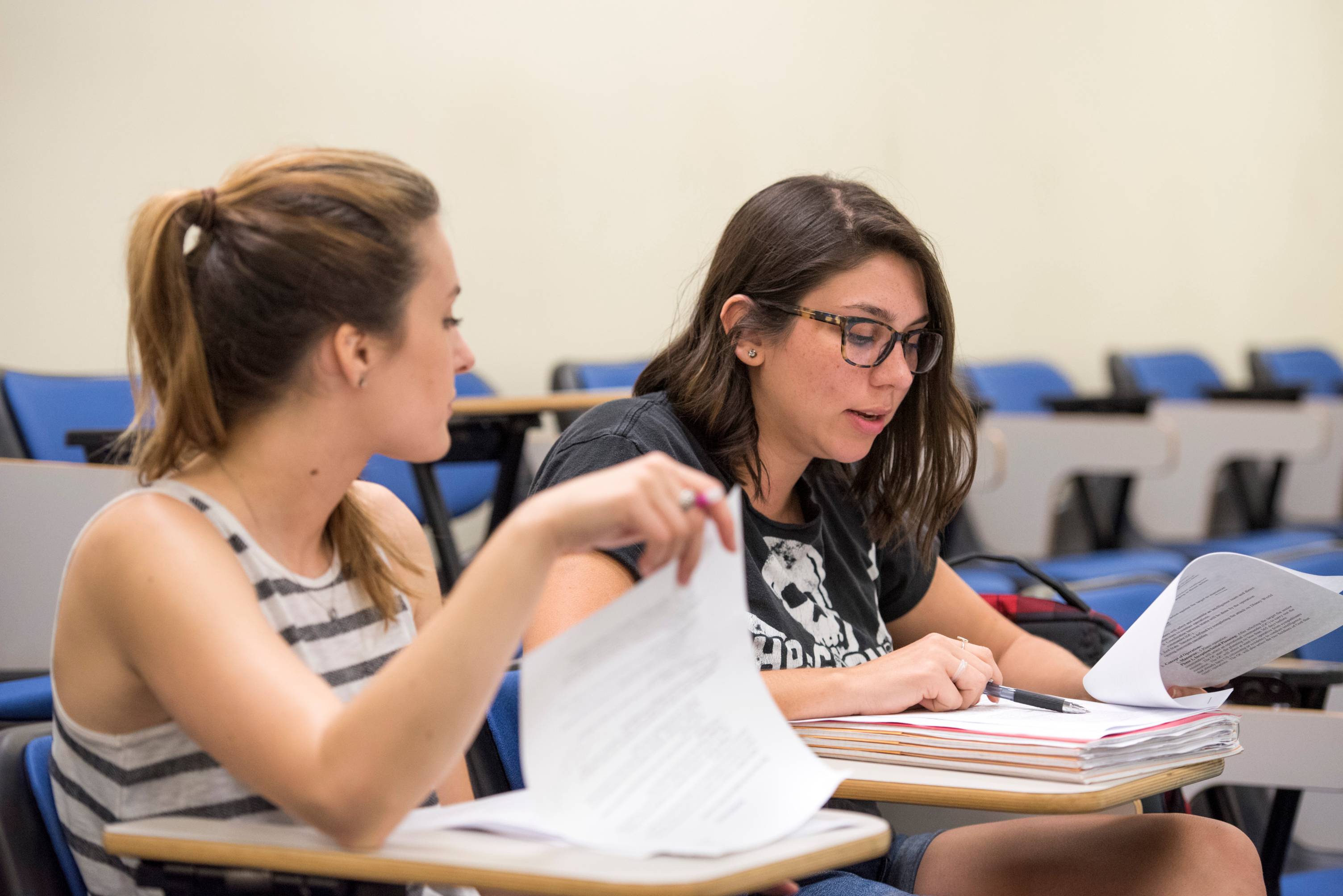 Two students in class discussing notes. 