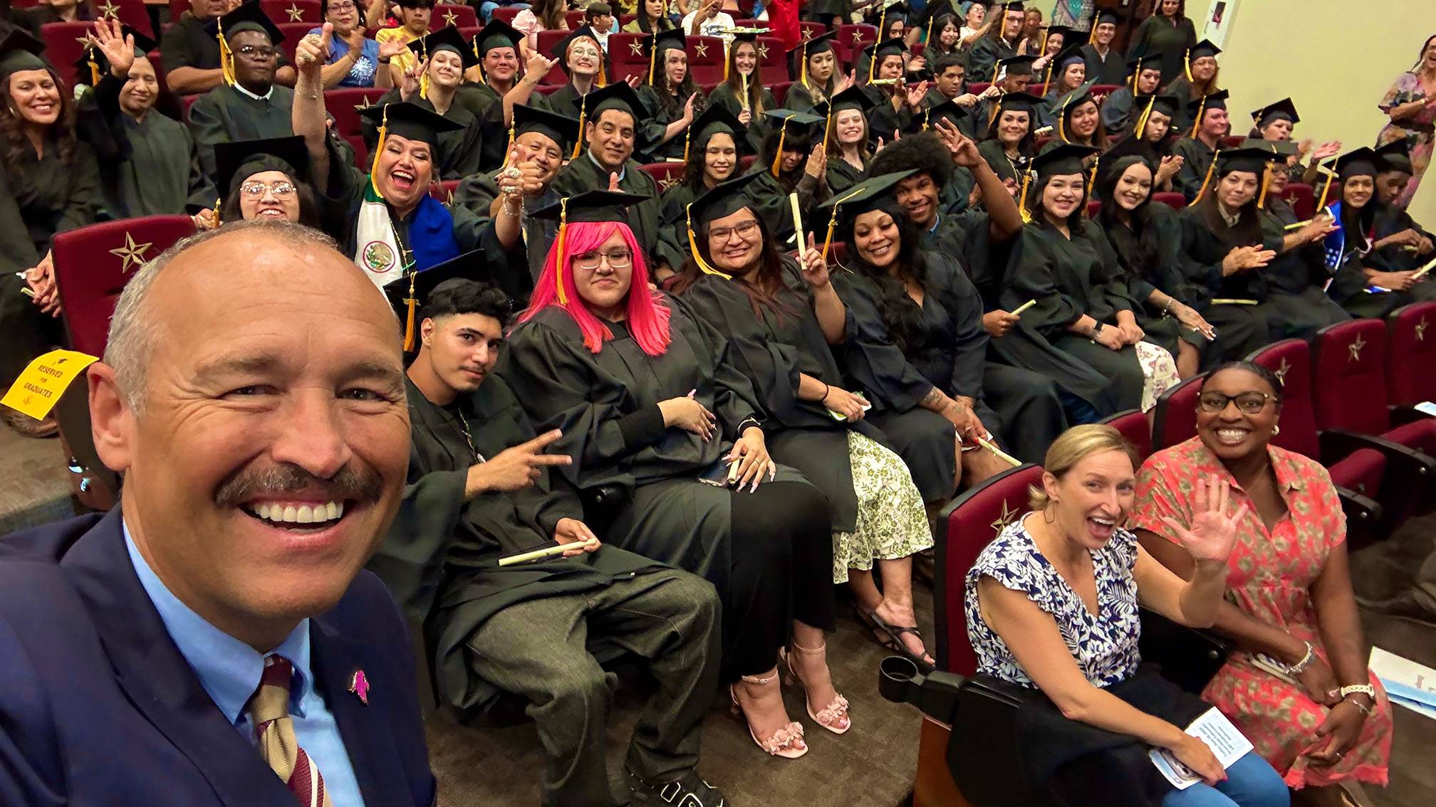 President Kelly Damphousse (left) poses for a photo with a large group of GED graduates.