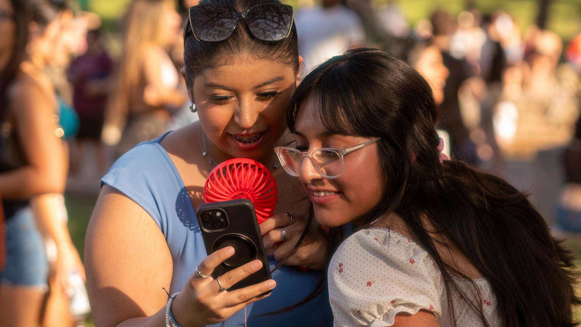 A young woman holds her phone up as her friend leans over her shoulder to see something on the screen.