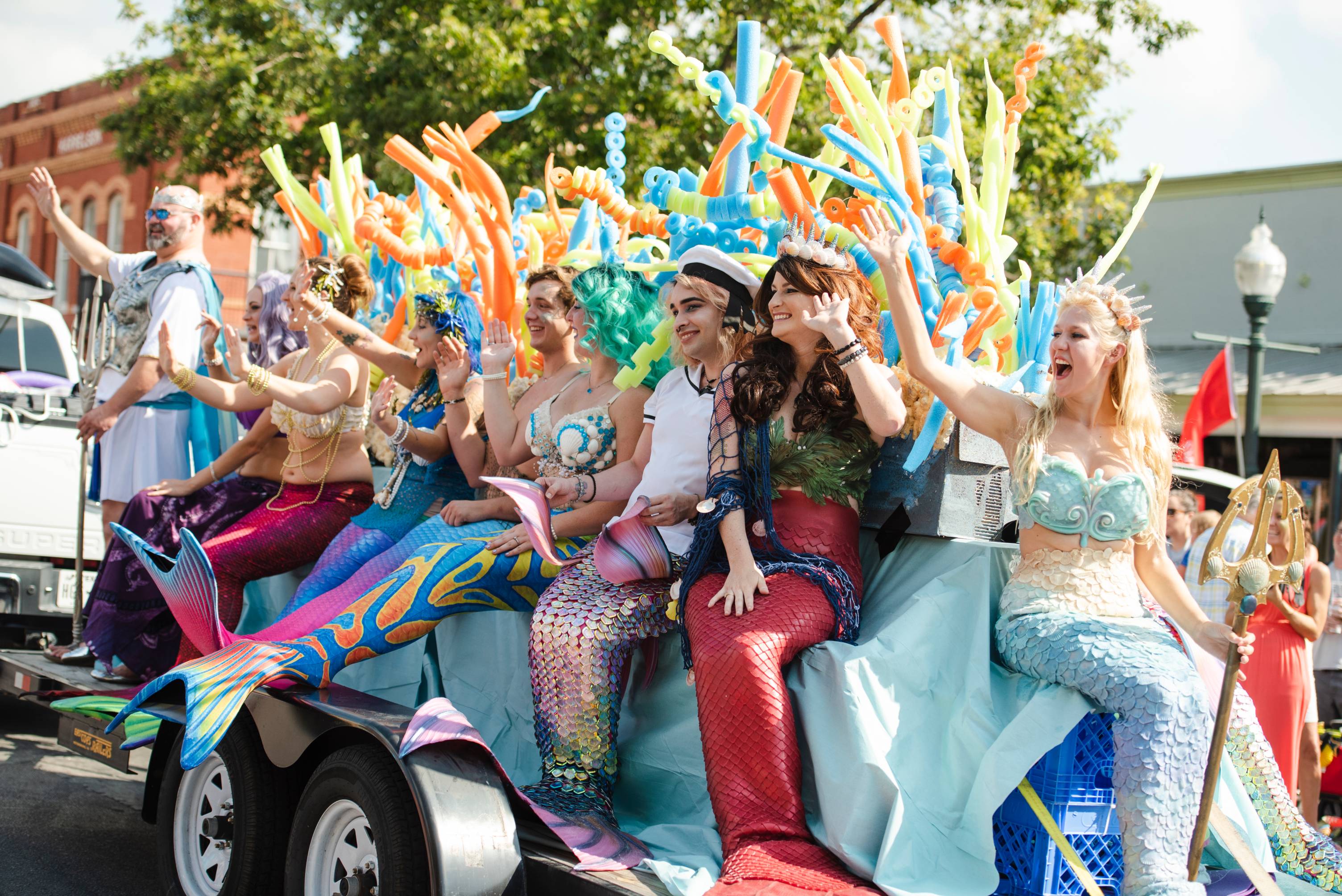 People in mermaid costumes sitting on a float in a parade at the mermaid festival