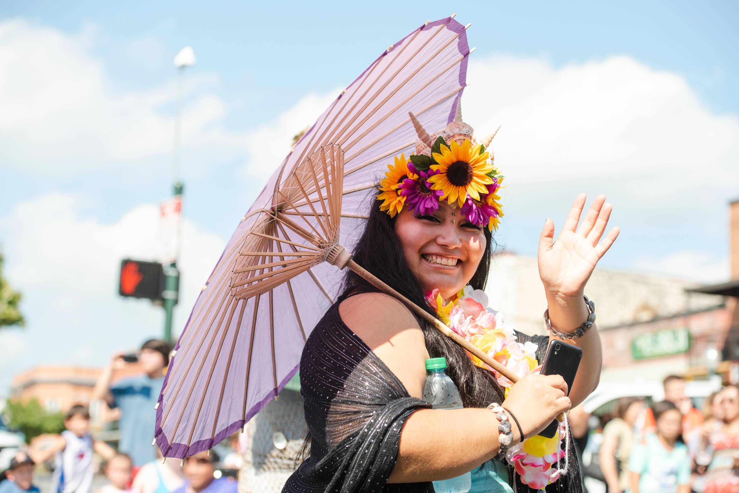Festive woman smiling and waving at the camera with her umbrella and flower crown