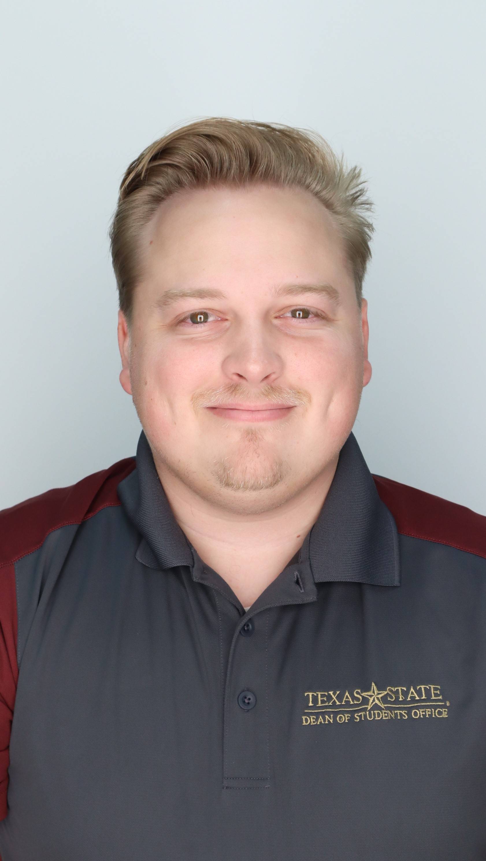 Connor headshot-smiling, wearing a gray and marroon dean of students shirt
