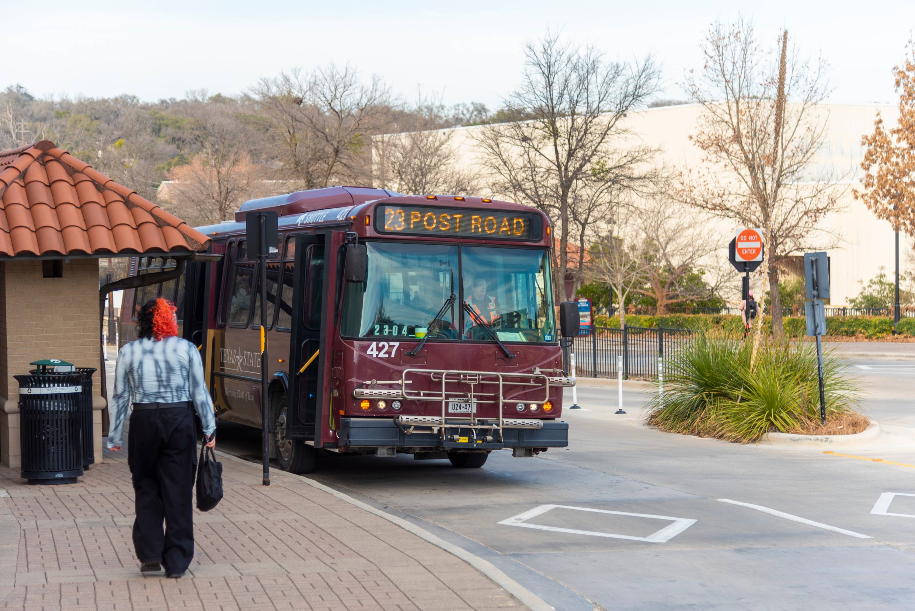 Shuttle stopped at the bus stop as a young woman walks towards to board