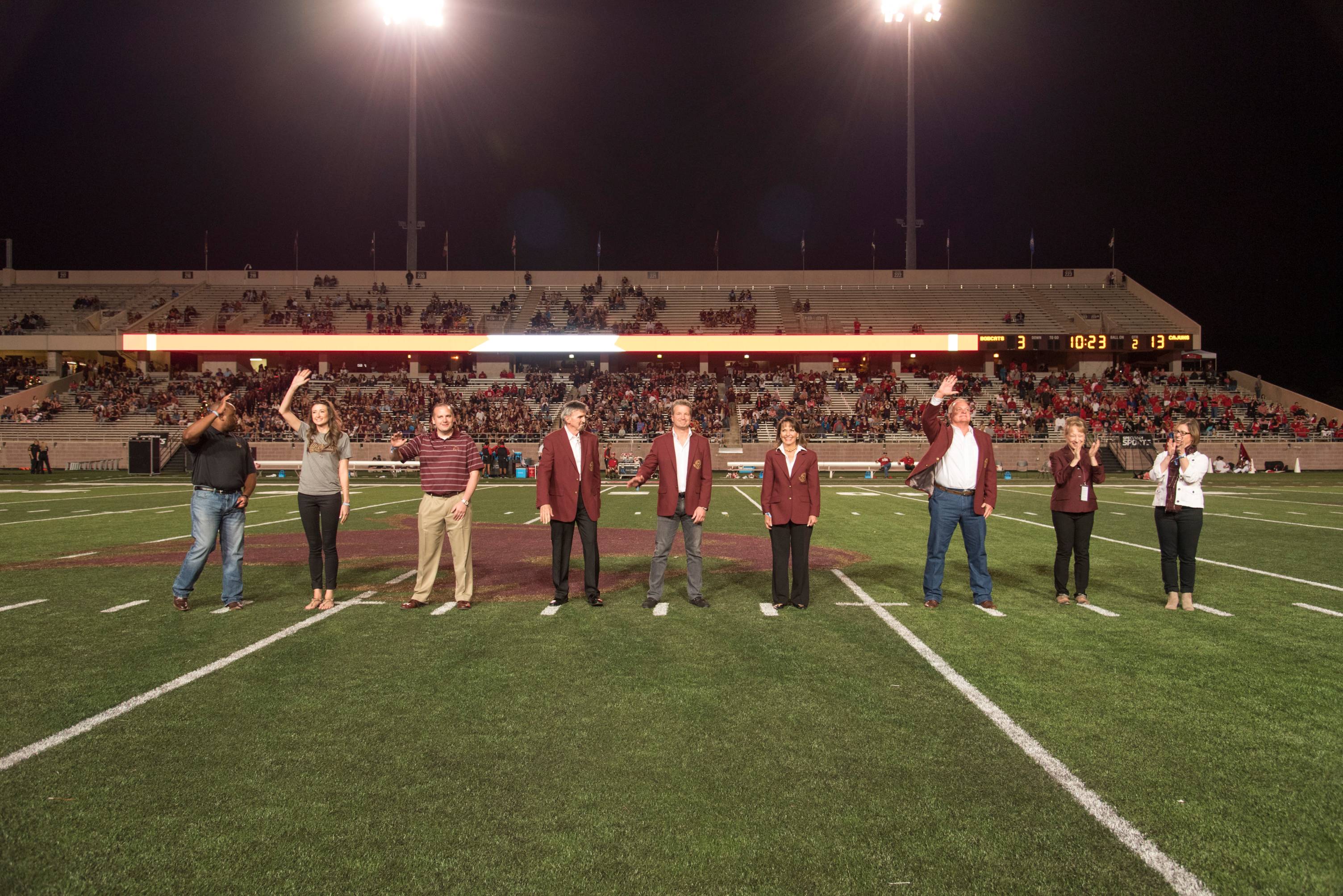 Photo of a group of alumni standing on a football field, posing