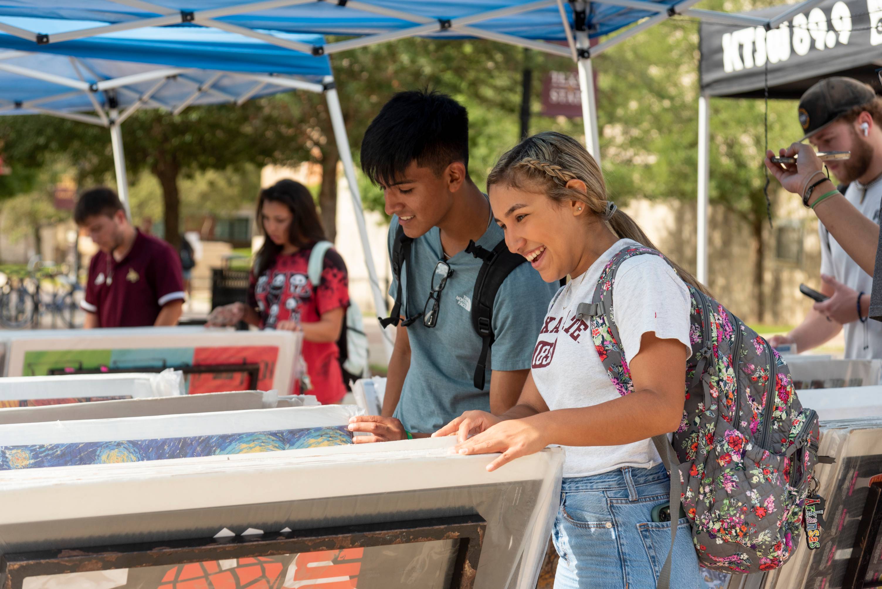 Imagine of students looking at items in an outdoor booth, smiling