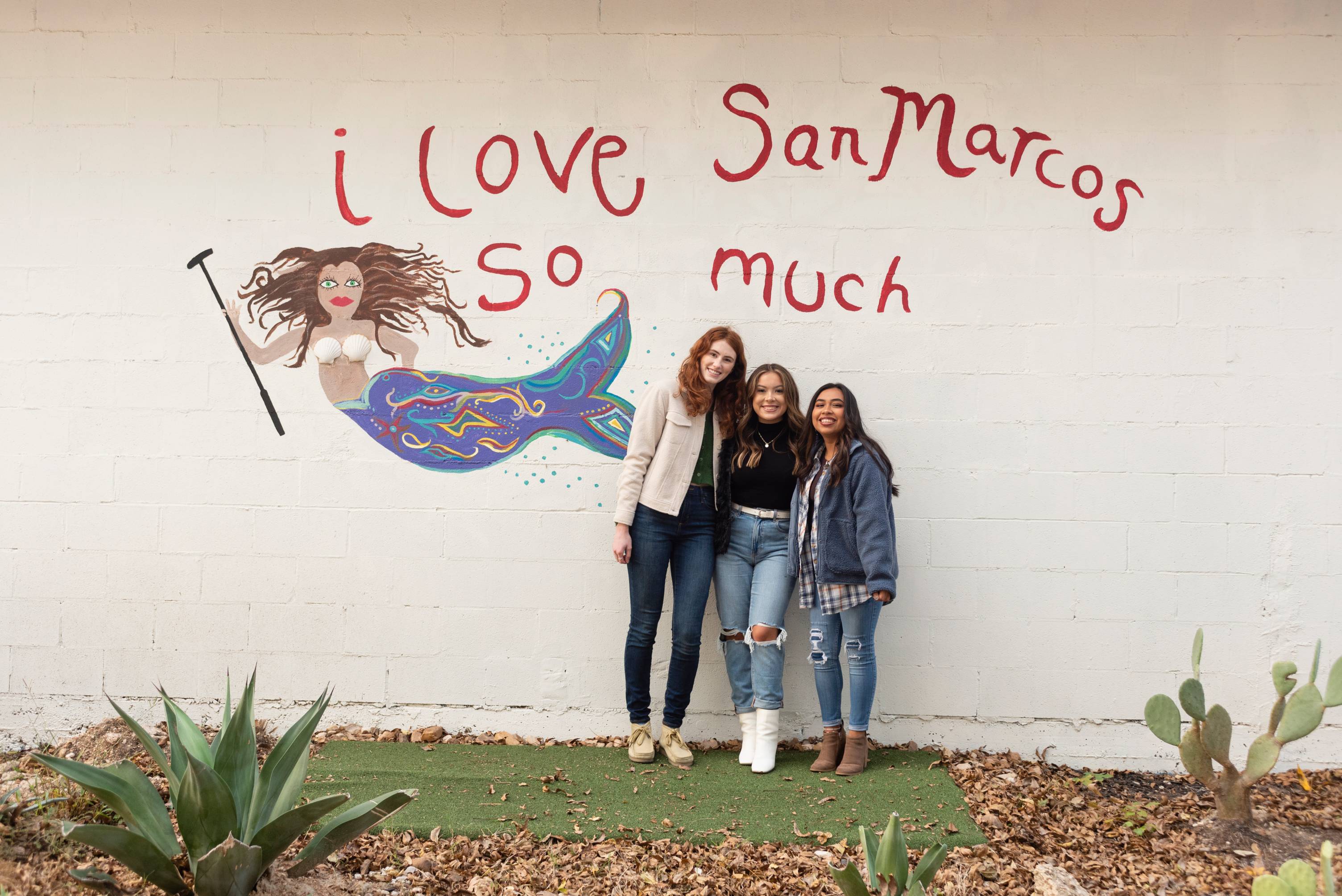 Photos of two people standing in front of a wall with writing on it that reads "I love San Marcos so much"