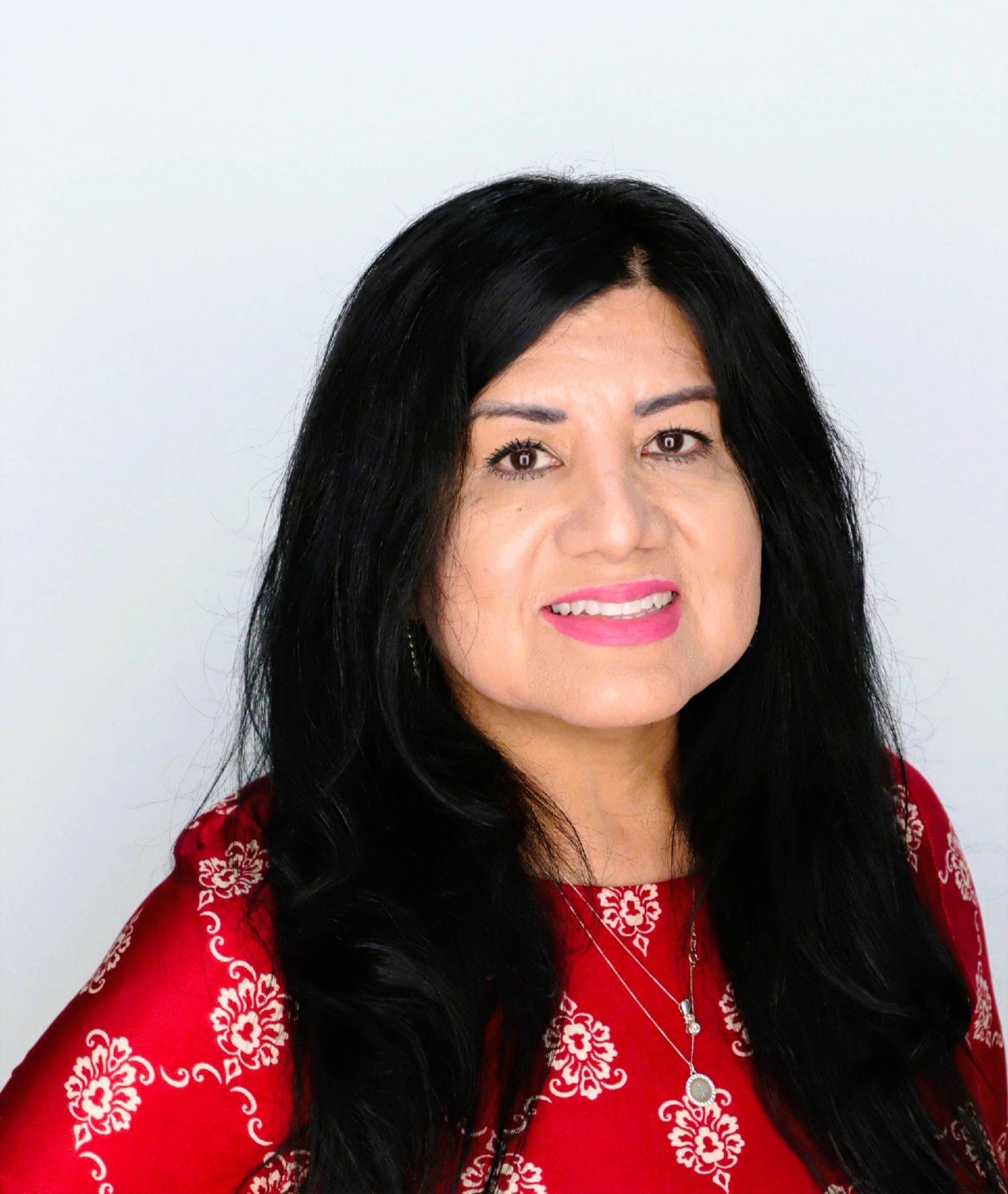 Alma Machado headshot, smiling wearing a red with floral dress