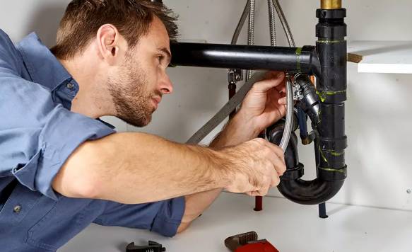 a okumber tightening a pipe under a sink