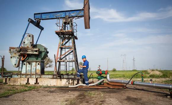 n oil worker in an oil field with oil derricks behind him