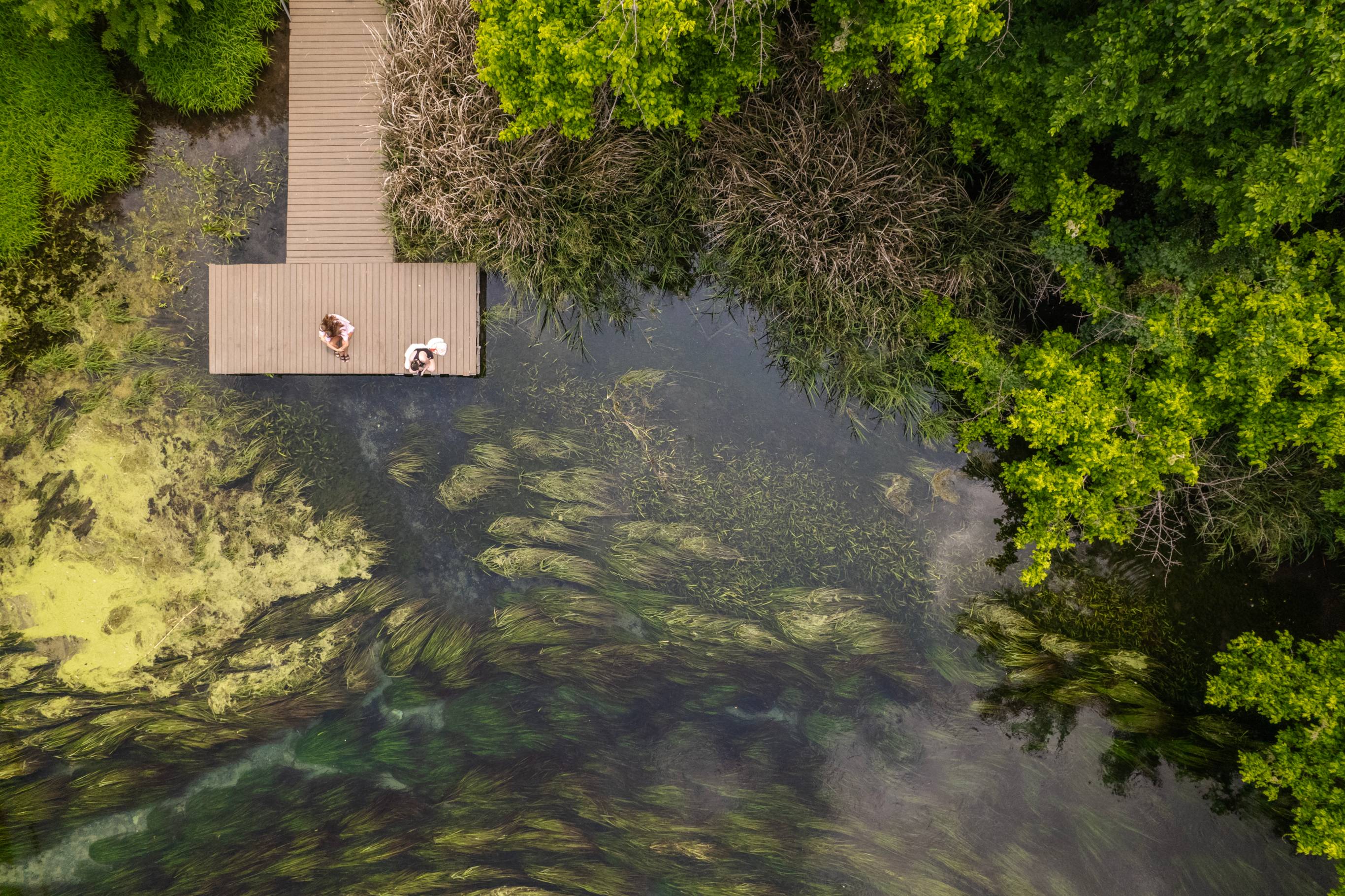 Aerial view of 2 people sitting on a dock at Sewell looking out at the river