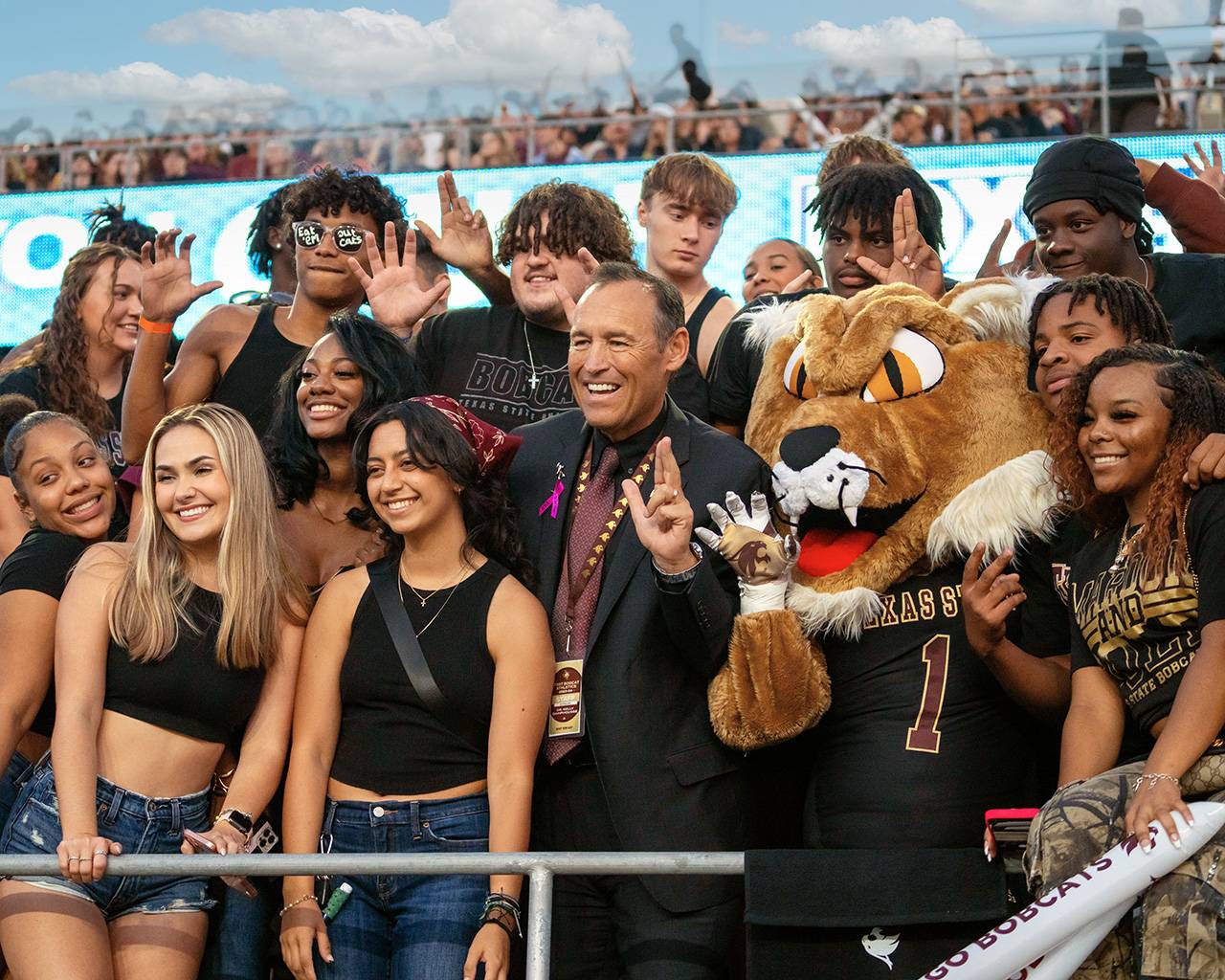 Group of students posing with TXST president and Boko at a Bobcat sports event