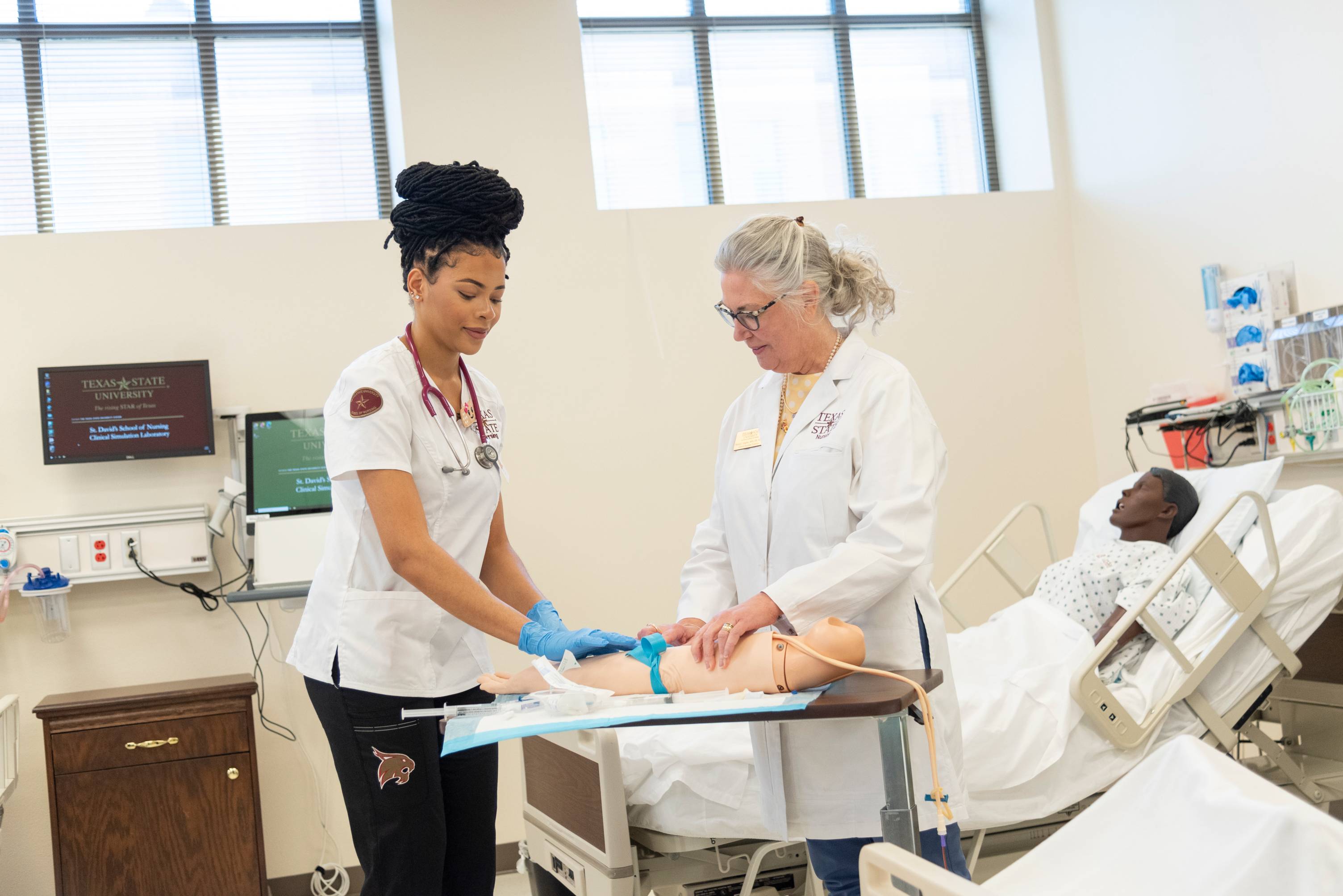 Nursing student and professor practicing administering an IV on a fake arm