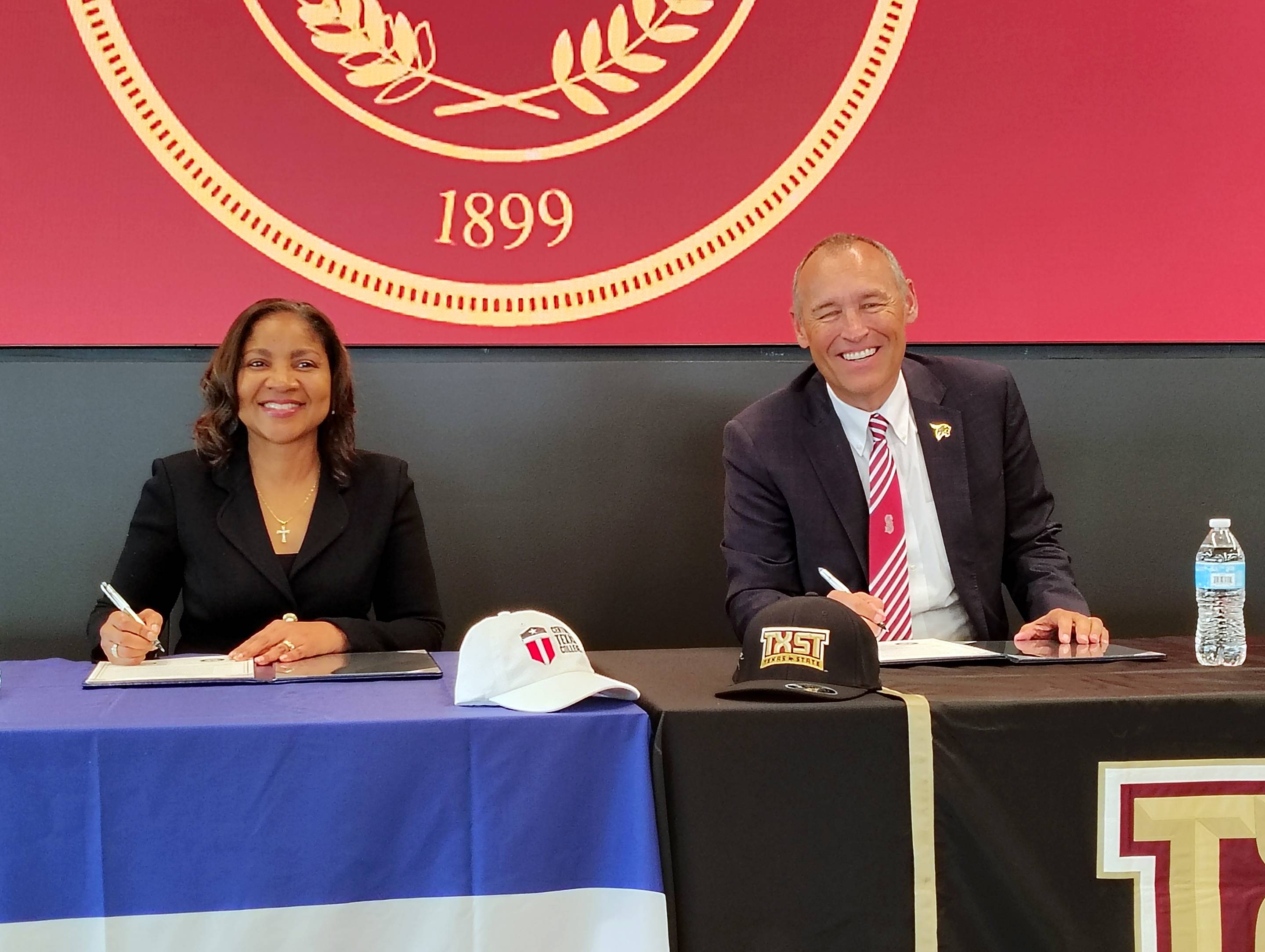 two people signing paperwork at a press conference