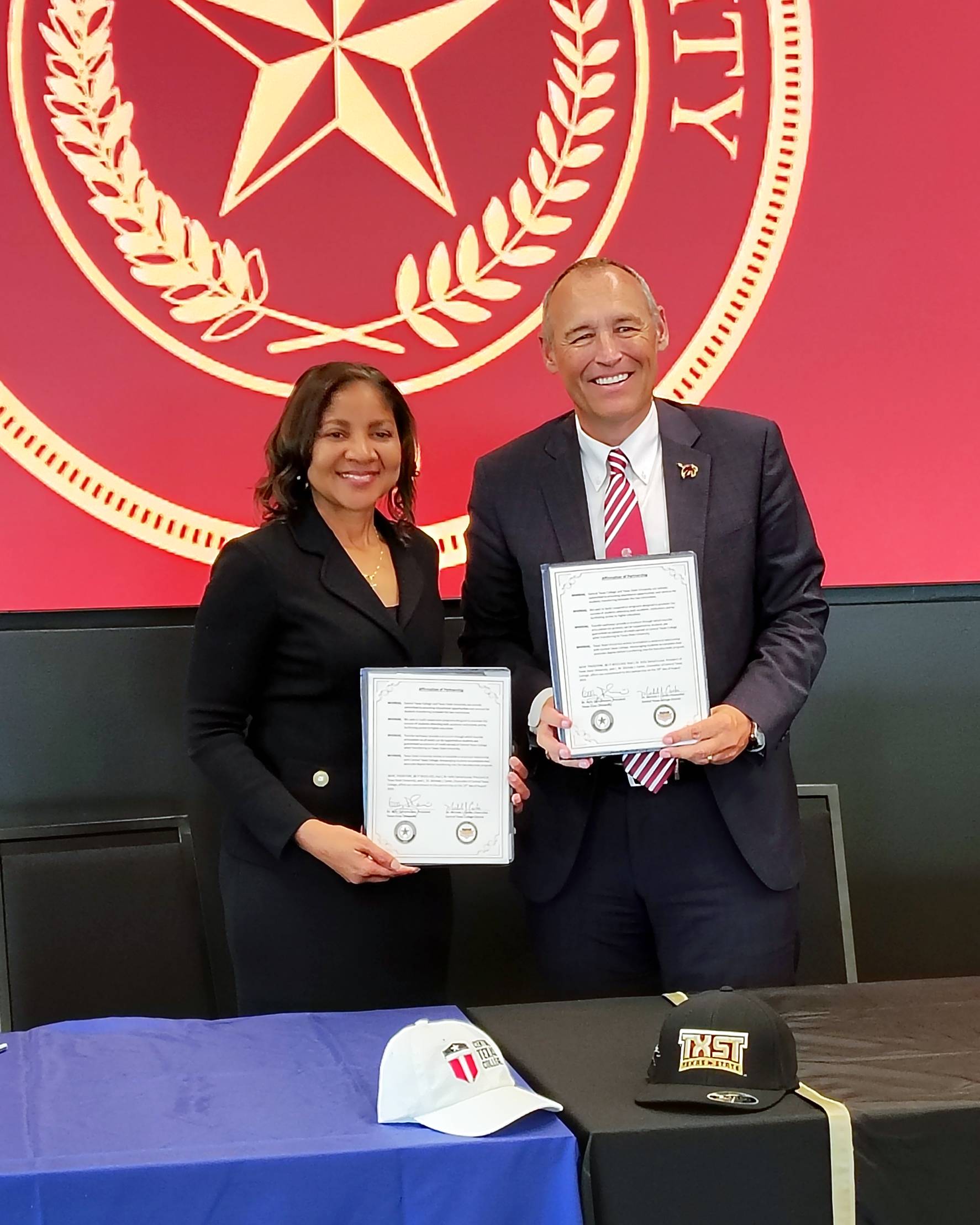 two people holding certificates at a signing ceremony